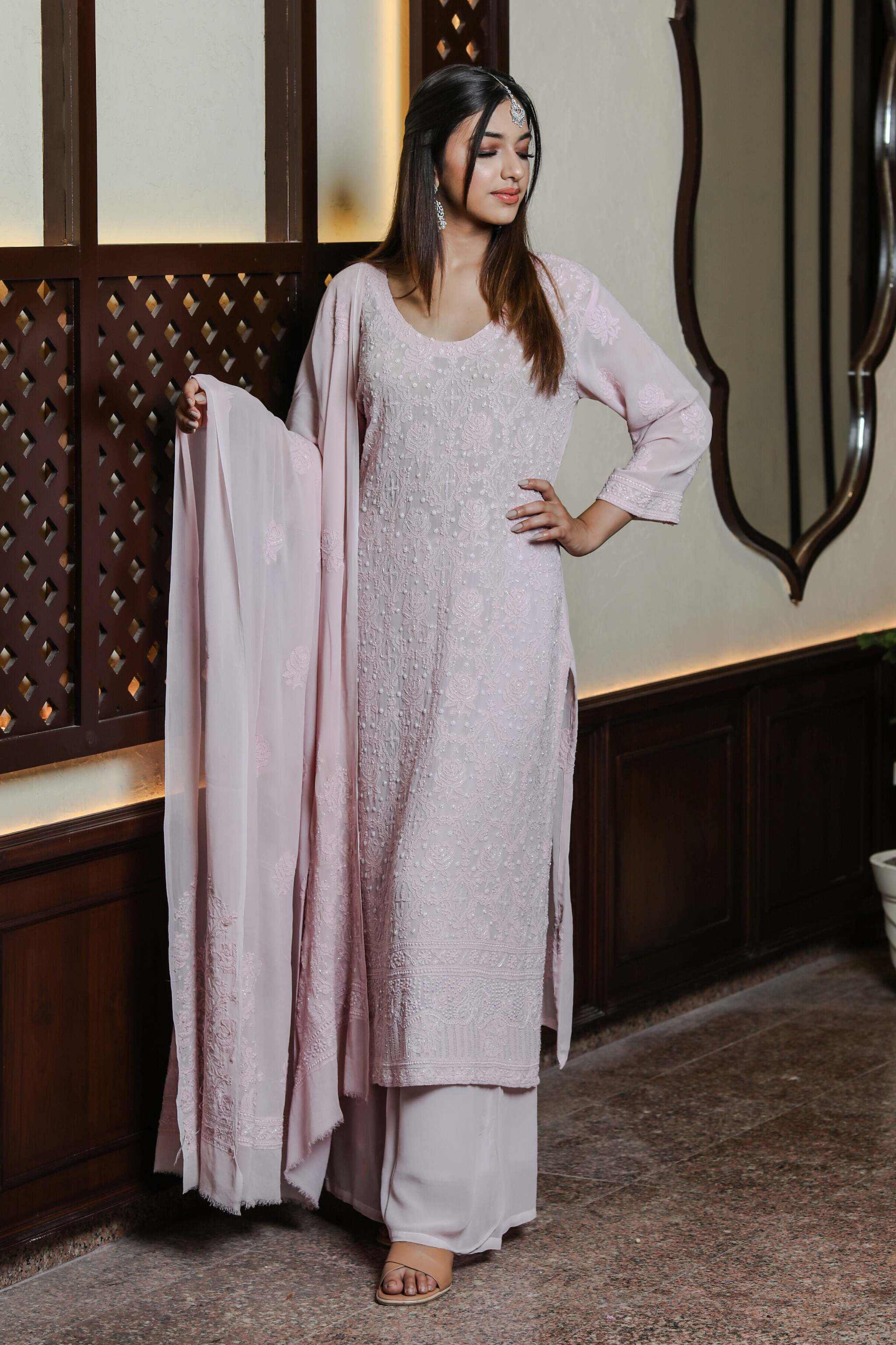 Woman in a light pink traditional Chaand Embroidered Wedding Suit standing indoors with decorative wall in the background