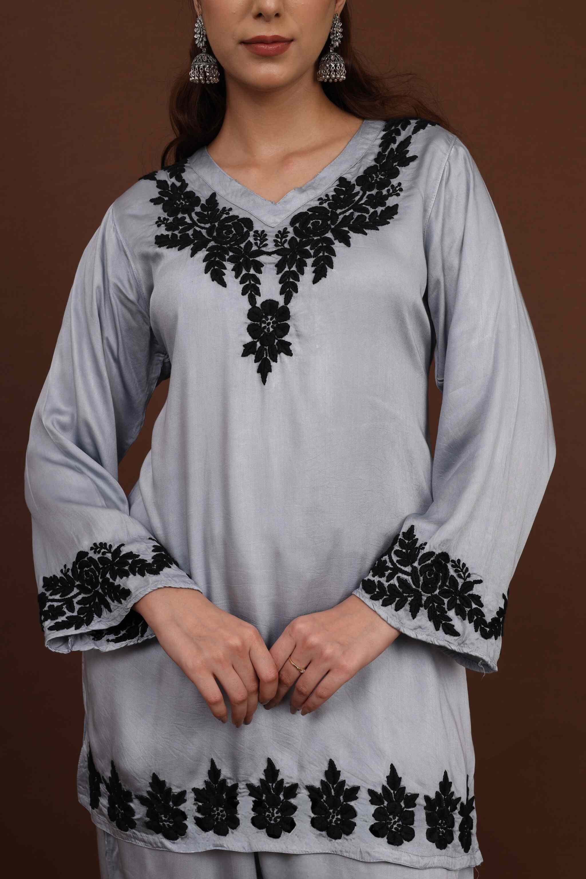 close up of chikankari embroidery of light gray long-sleeve co ord set with black floral embroidery on a brown background