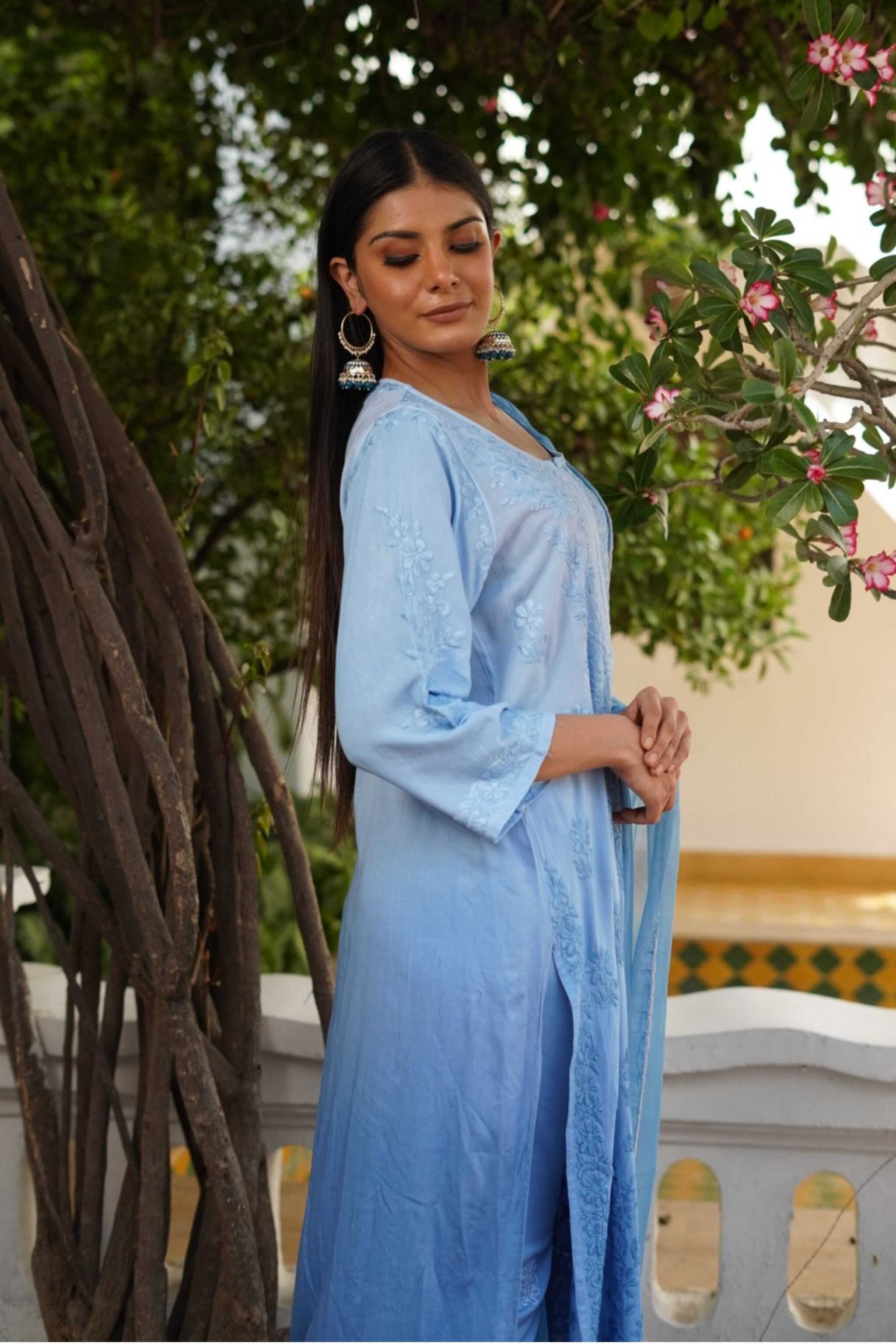 Woman in a light blue traditional chikankari kurta set standing outdoors with greenery in the background