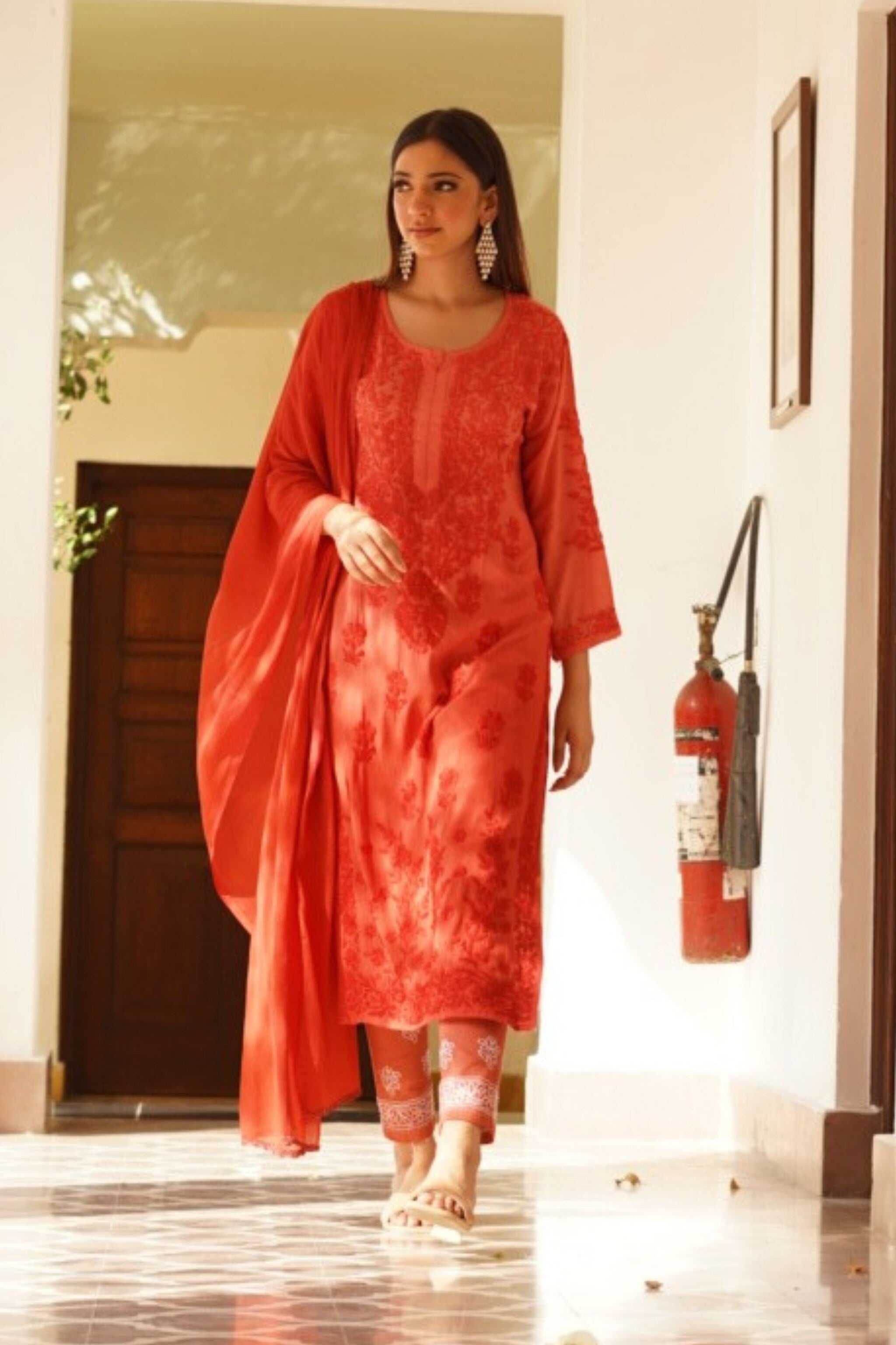 Woman in a red chikan kurta set standing in a hallway with a fire extinguisher visible.