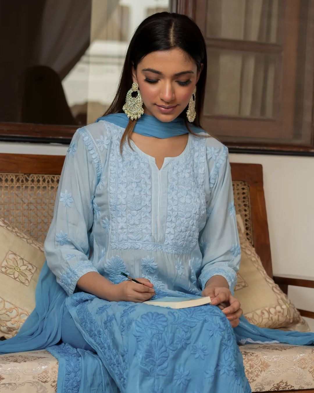 A women wearing a blue chikan kurta set sitting on a wooden bench