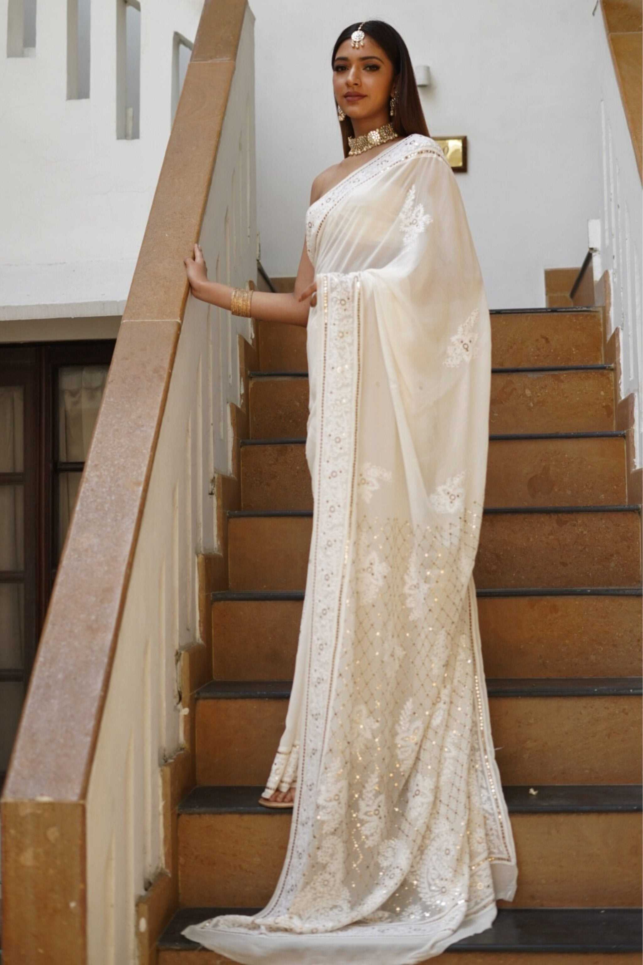 Woman in a white georgette saree with chikankari embroidery standing on a staircase
