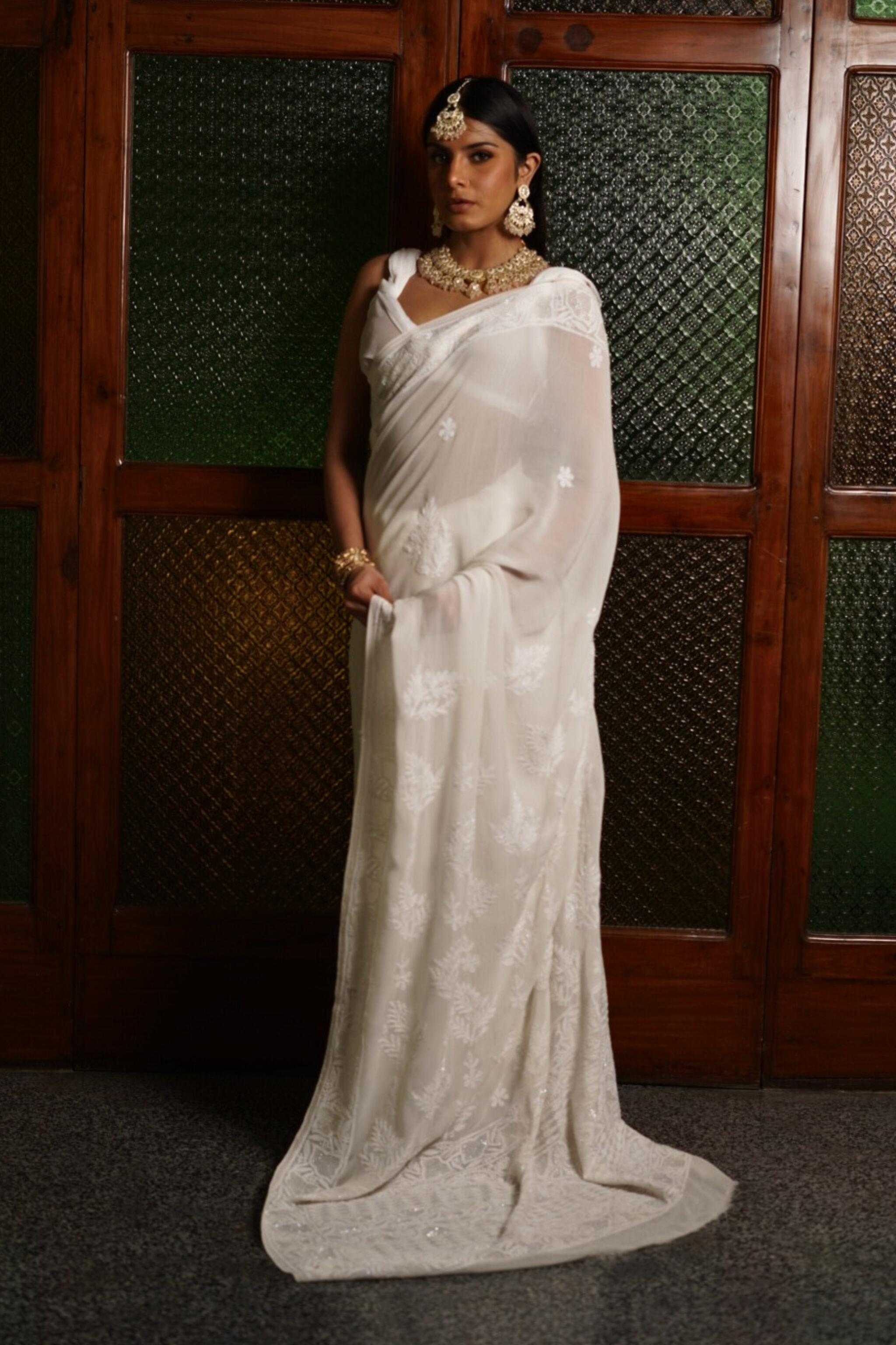 Woman in a white georgette chikankari saree with a matching blouse against a wooden panel background
