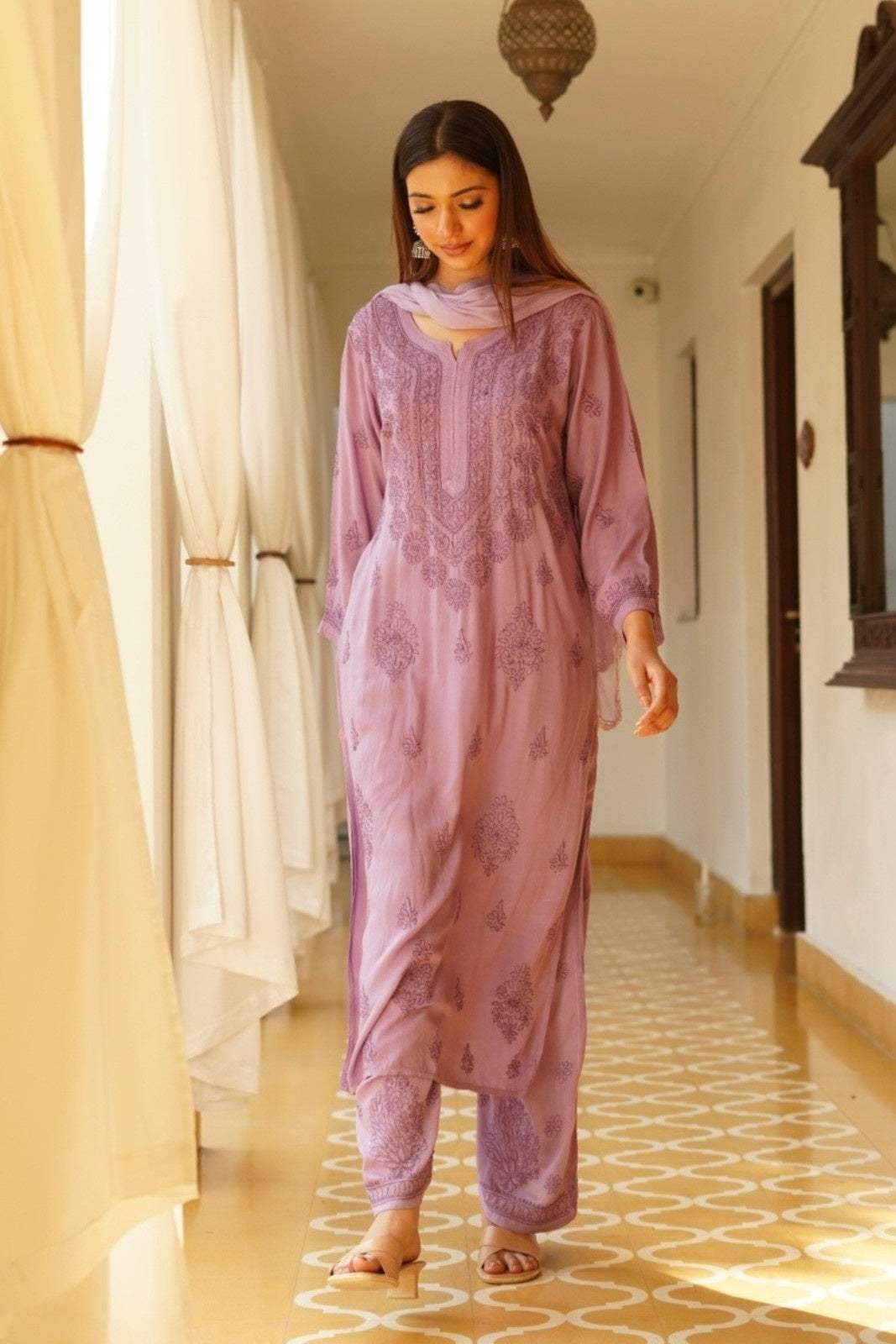 Woman in a pink traditional Mahek Purple Chikankari Suit Set standing in a room with patterned floor and white curtains.