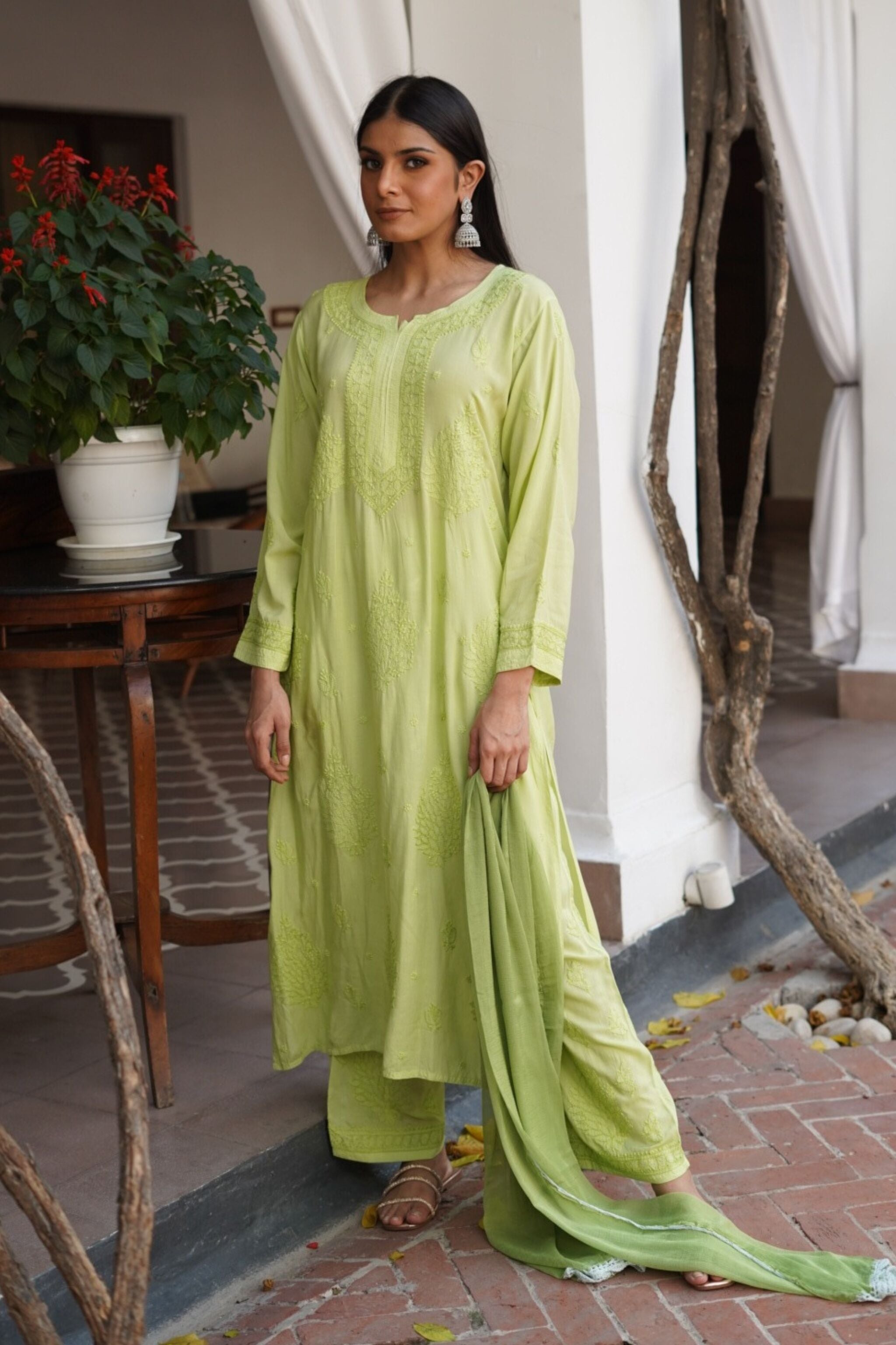 Woman wearing a light green traditional chikan kurta set standing in an indoor setting with plants and decor.