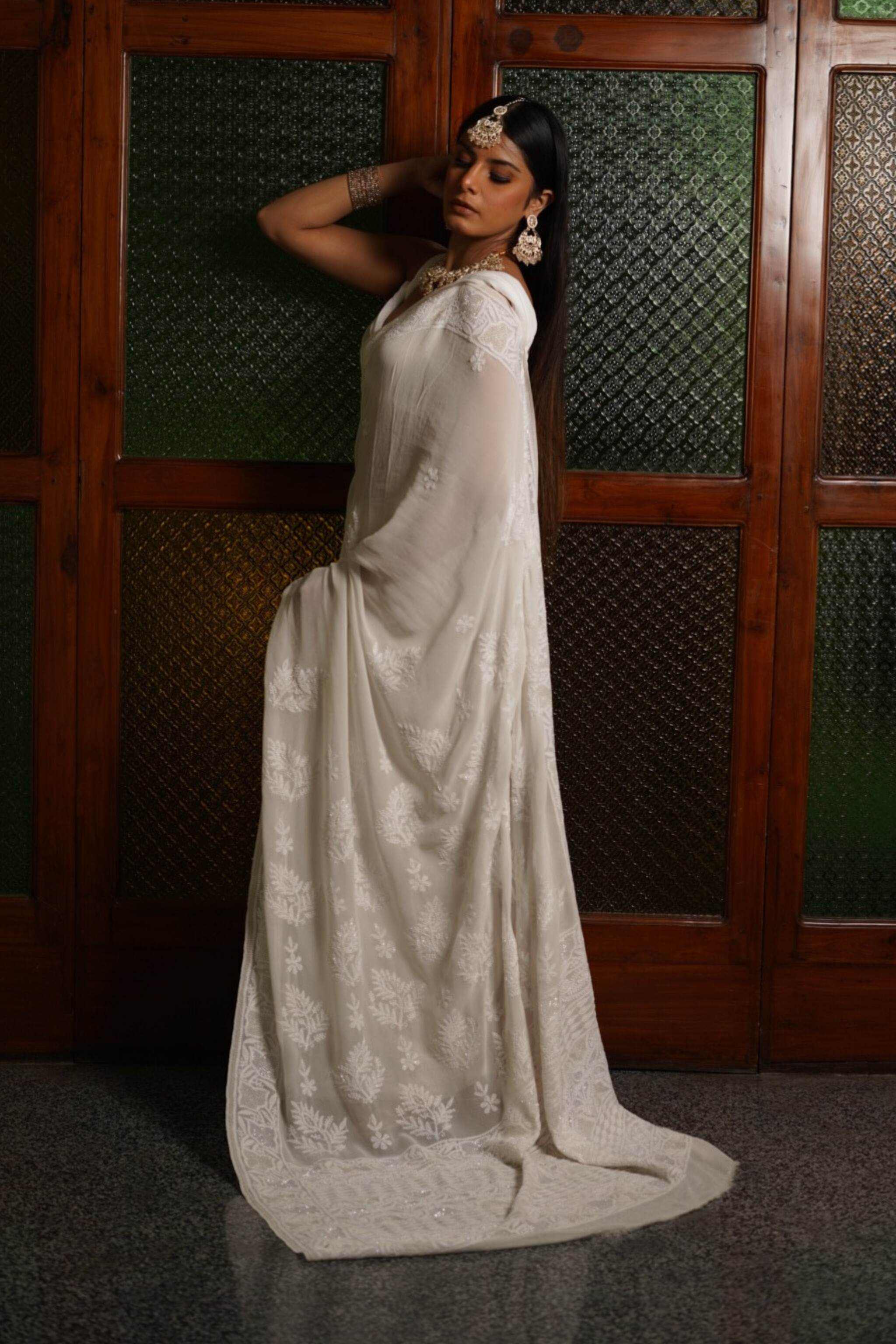 Woman in a white georgette chikankari saree with a floral headpiece against a wooden panel background