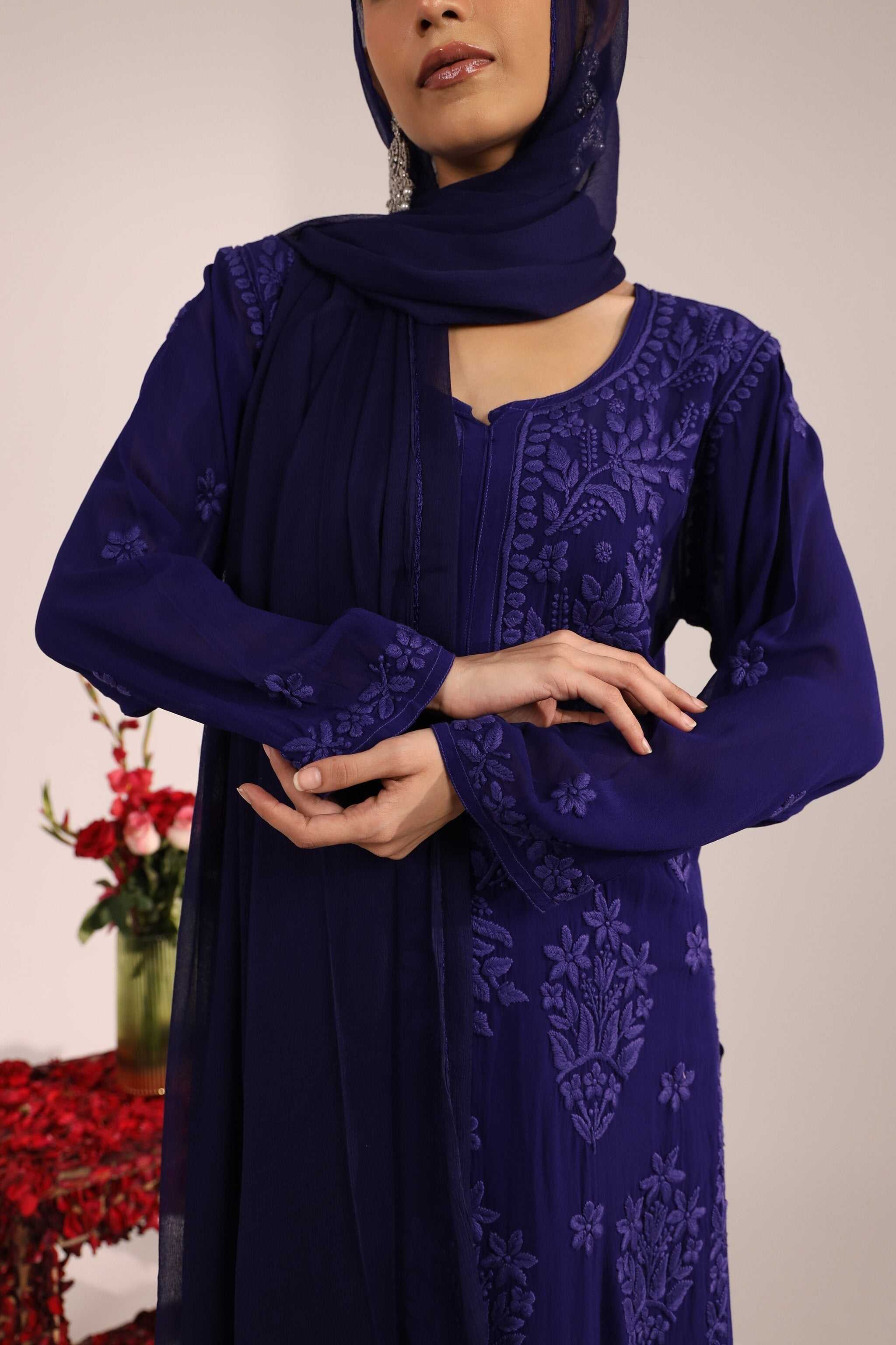 Woman wearing a dark blue embroidered dress with a matching dupattaagainst a neutral background.
