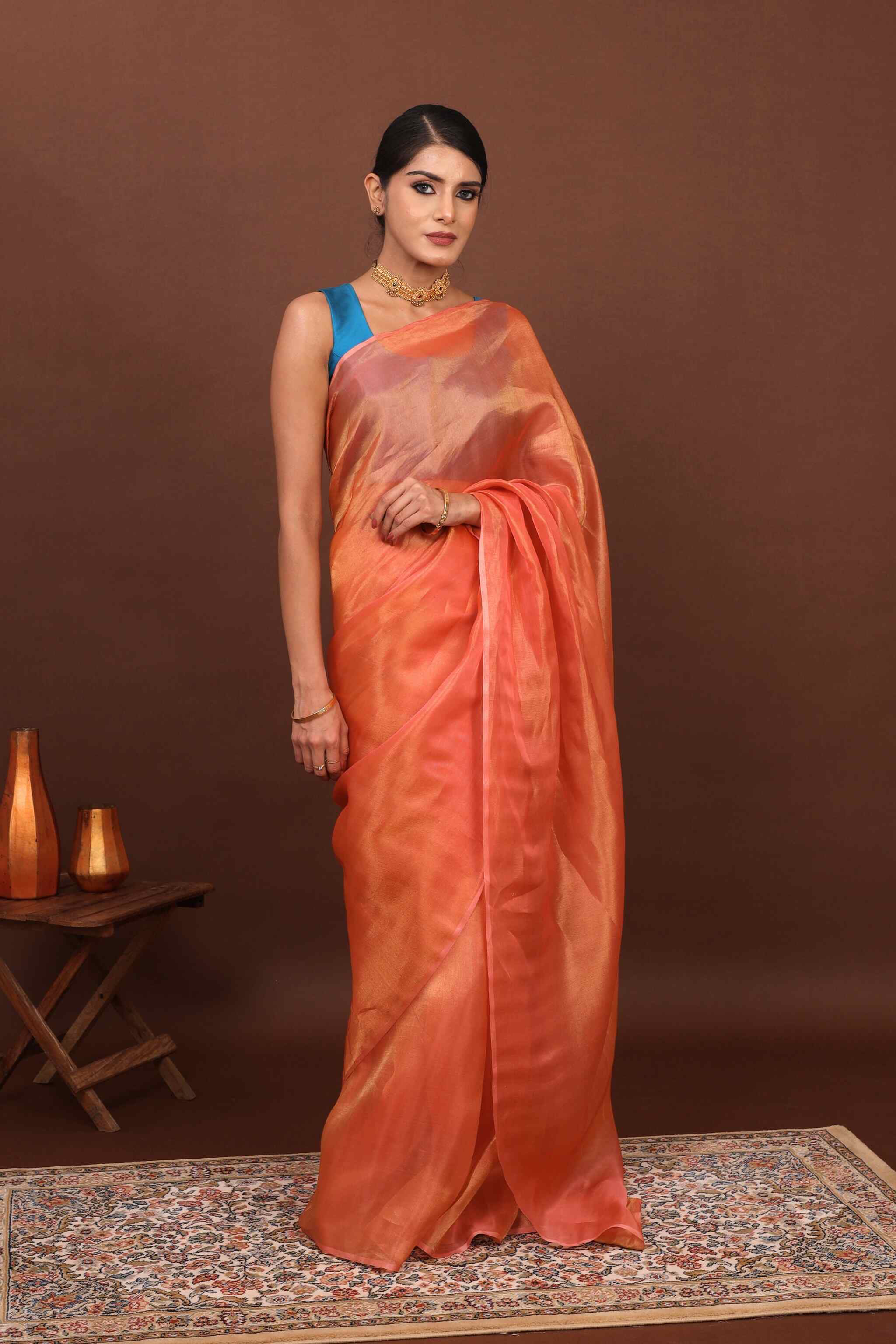 Woman wearing an orange tissue silk saree with a blue blouse against a brown background