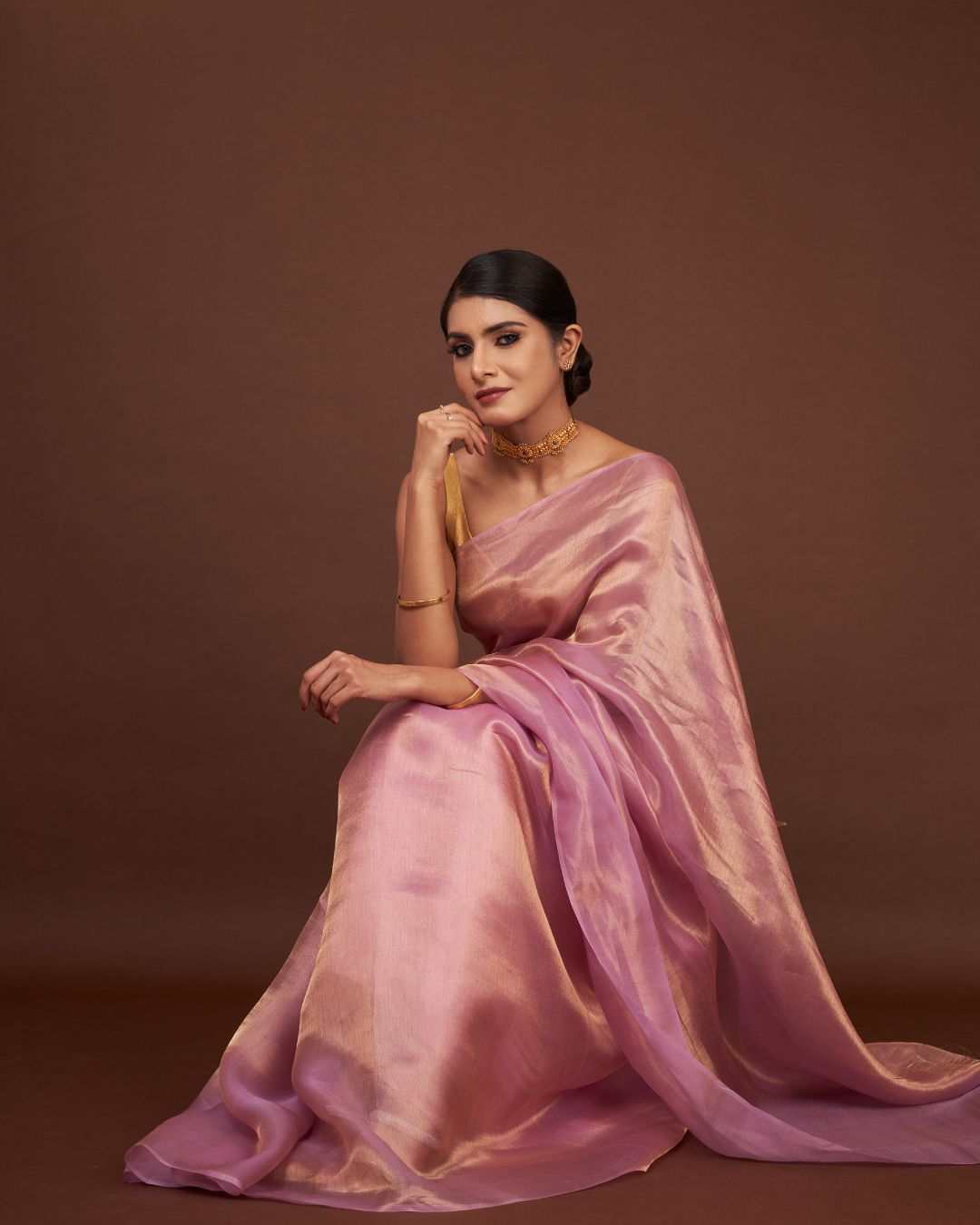 Sitting pose of model wearing Whisper Rose Gold tissue saree with soft lighting.