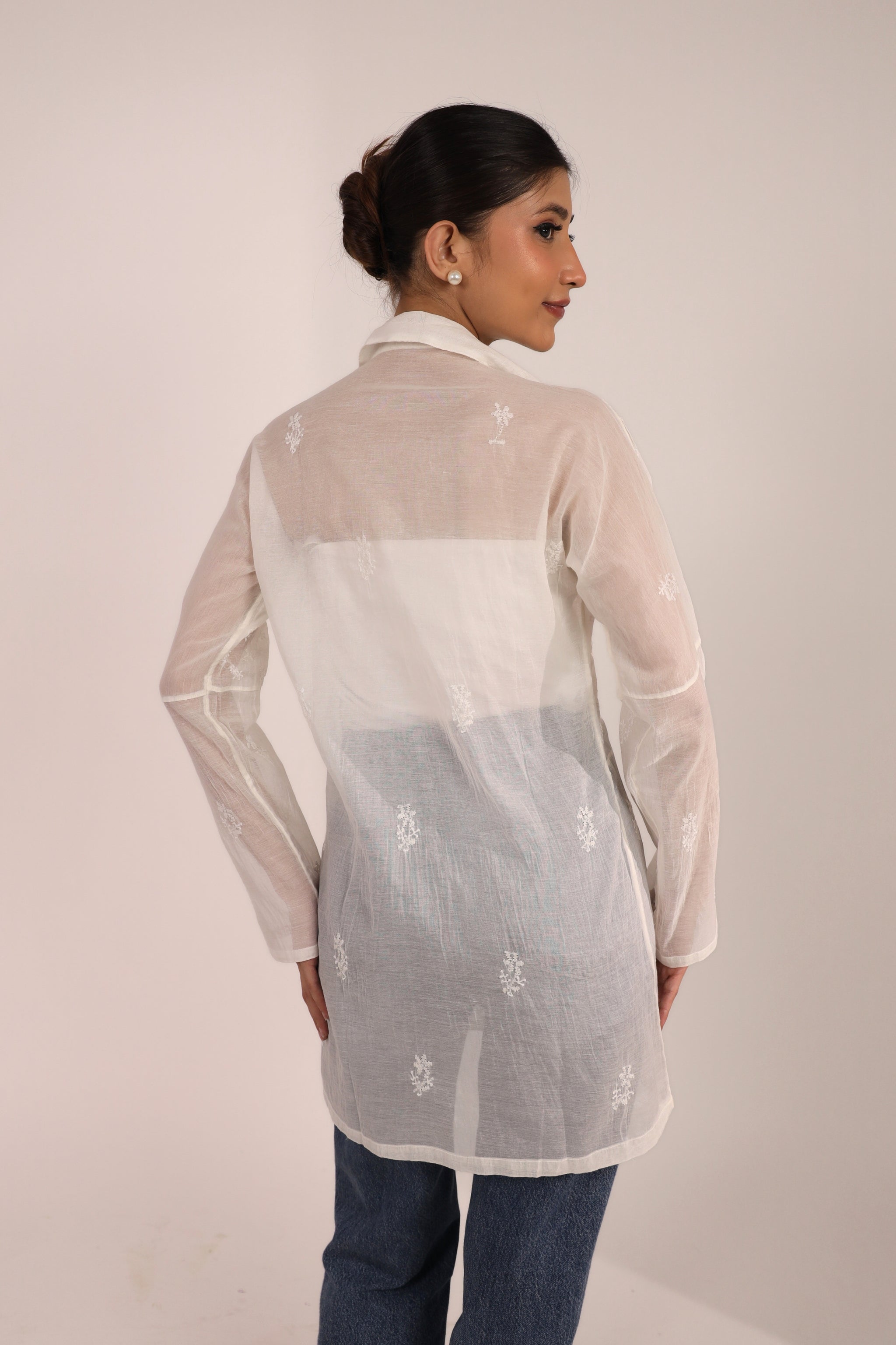 Woman wearing a sheer white embroidered Chikankari short kurti with a plain background