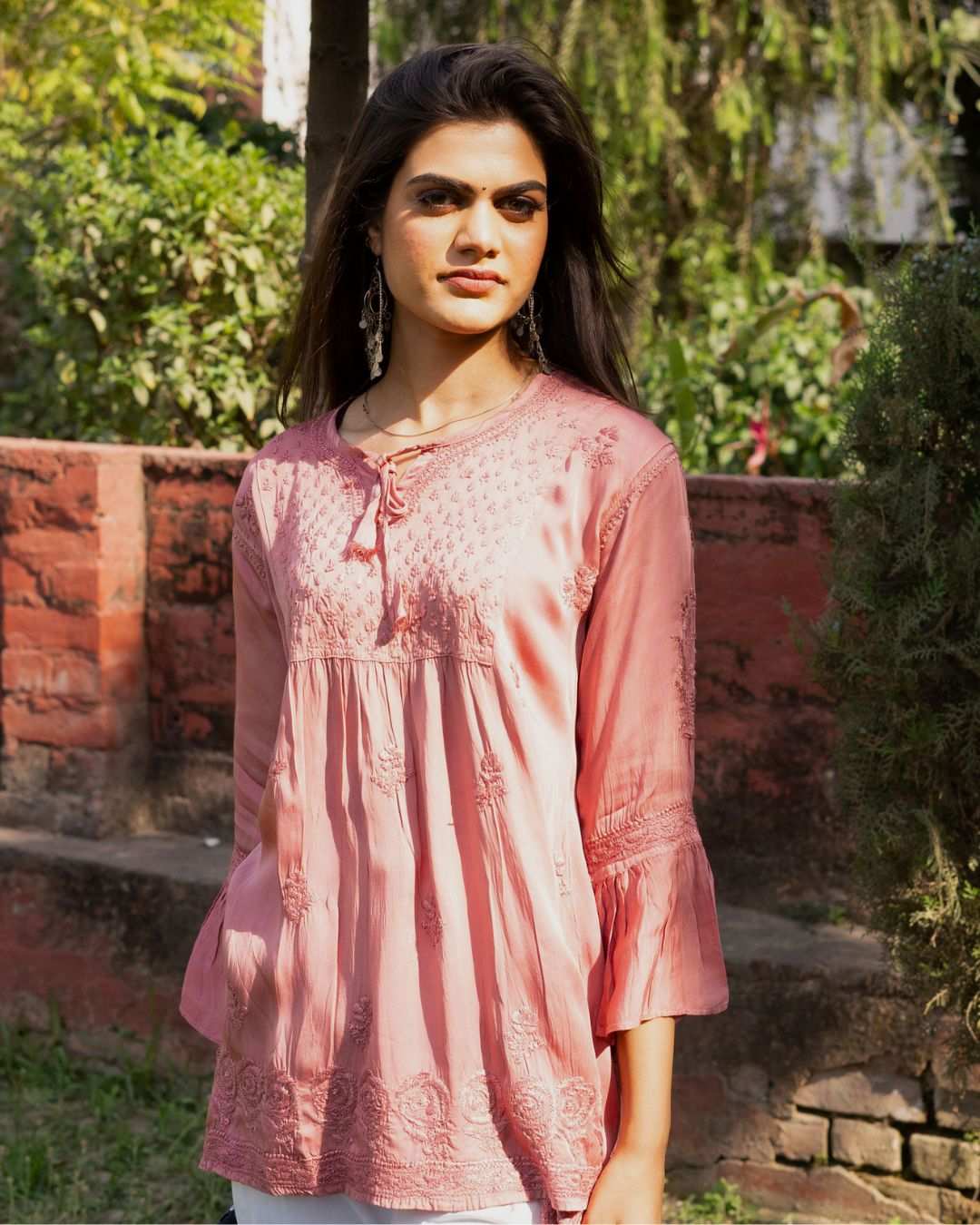 Women wearing pink short kurti with full bell sleeves made of modal satin fabric