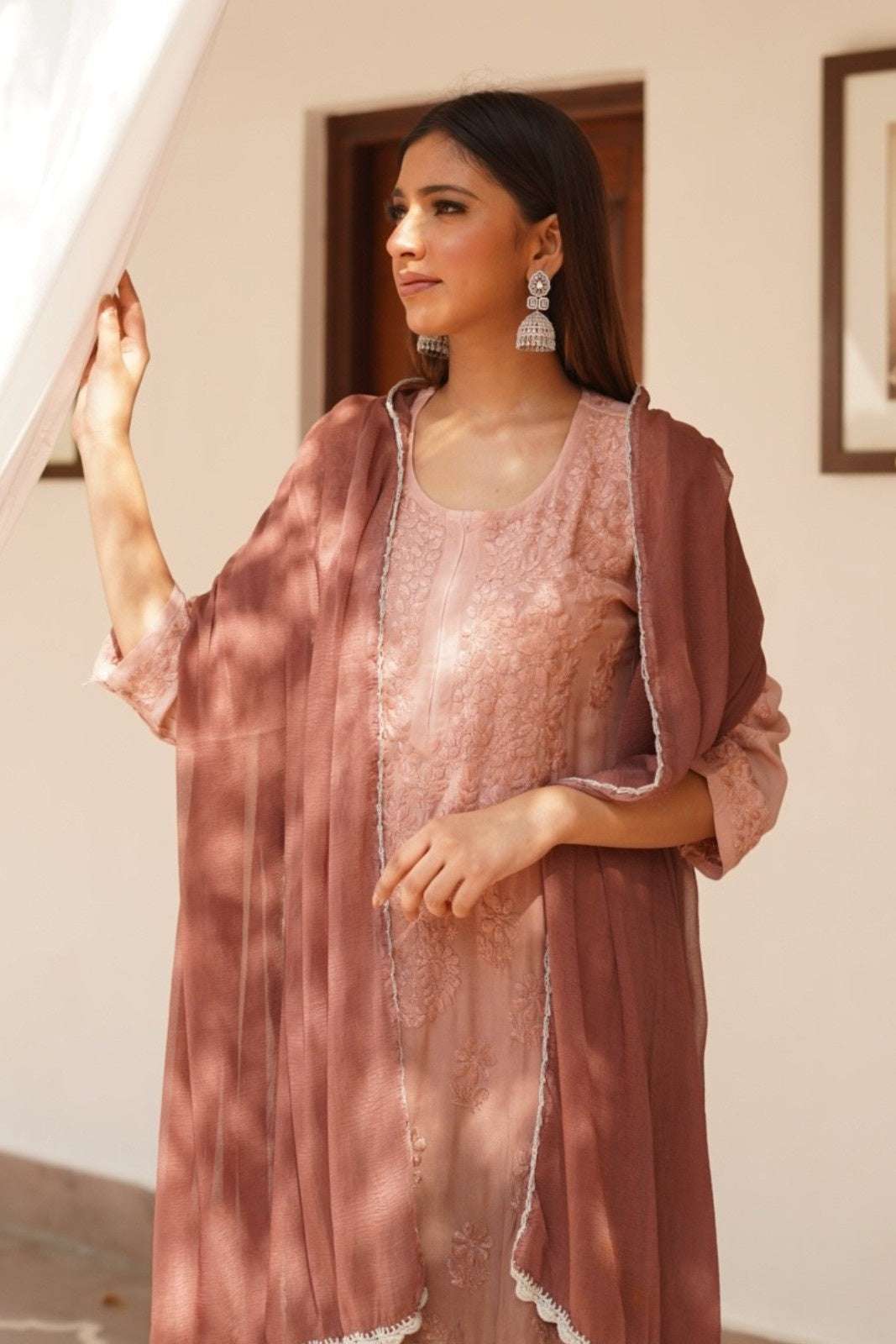 Woman wearing a pink traditional chikankari kurta set with a matching dupatta indoors.