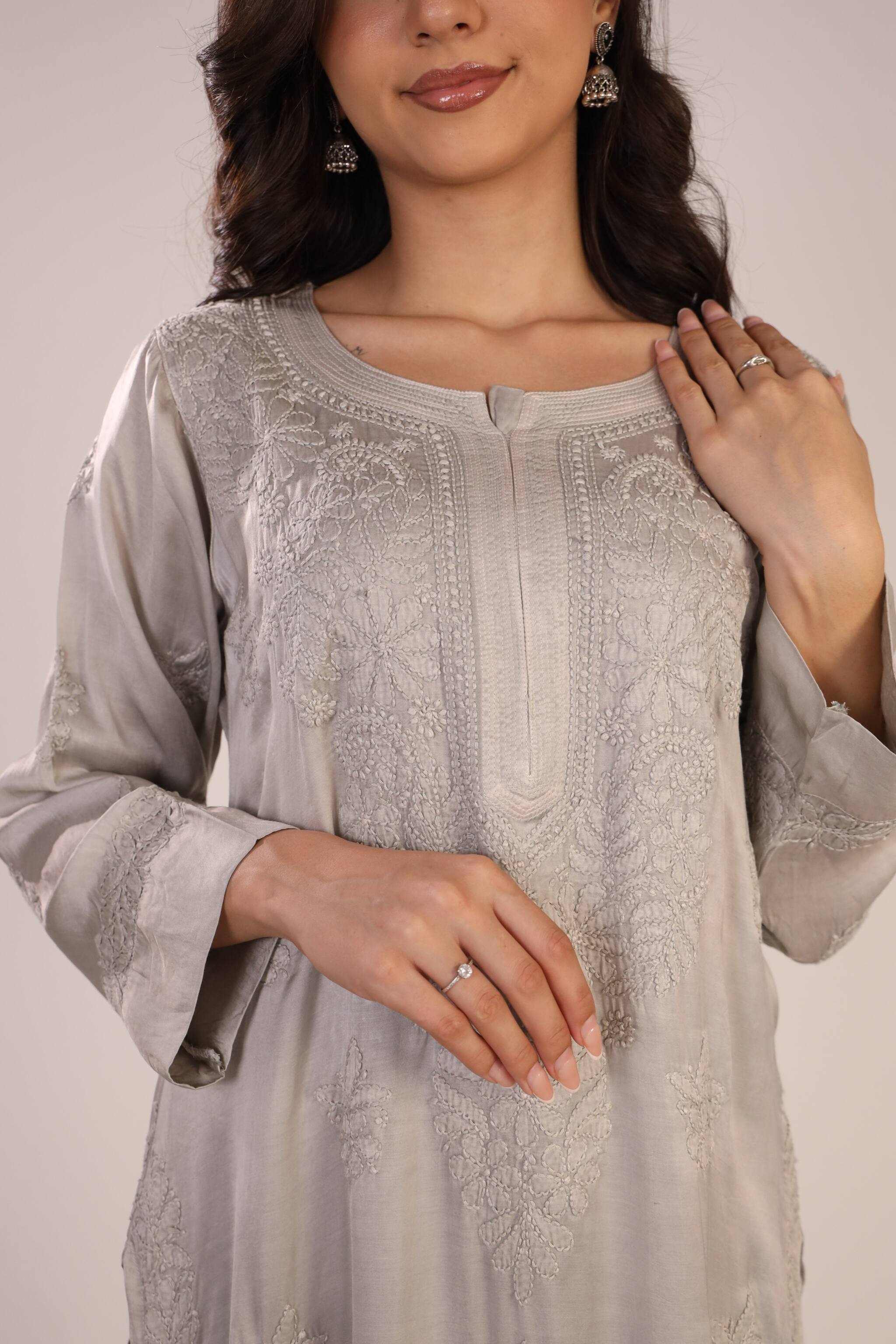 Woman wearing a light gray embroidered chikankari kurta with a plain background