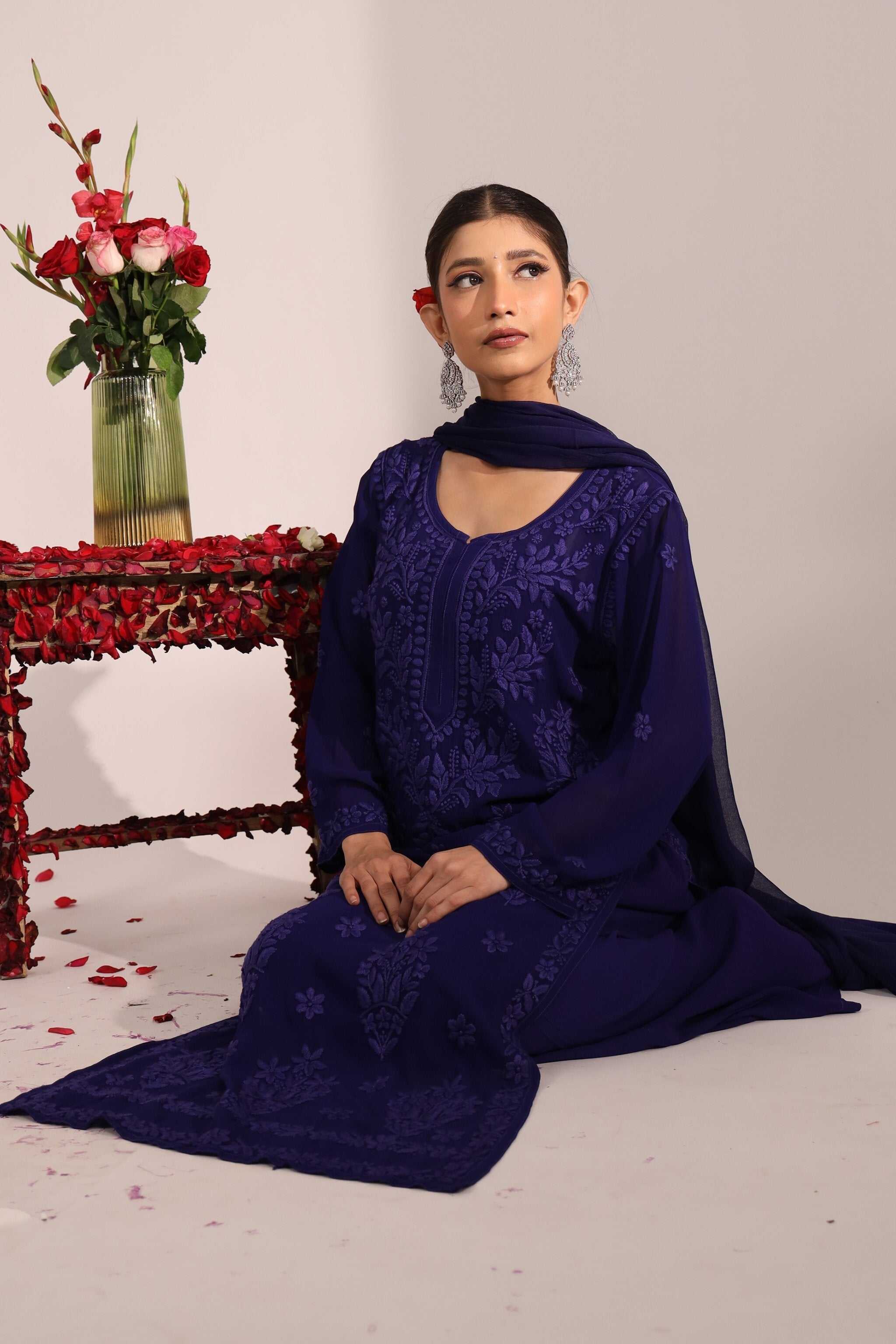 Woman in a blue embroidered chikan suit sitting on the floor with a vase of flowers in the background