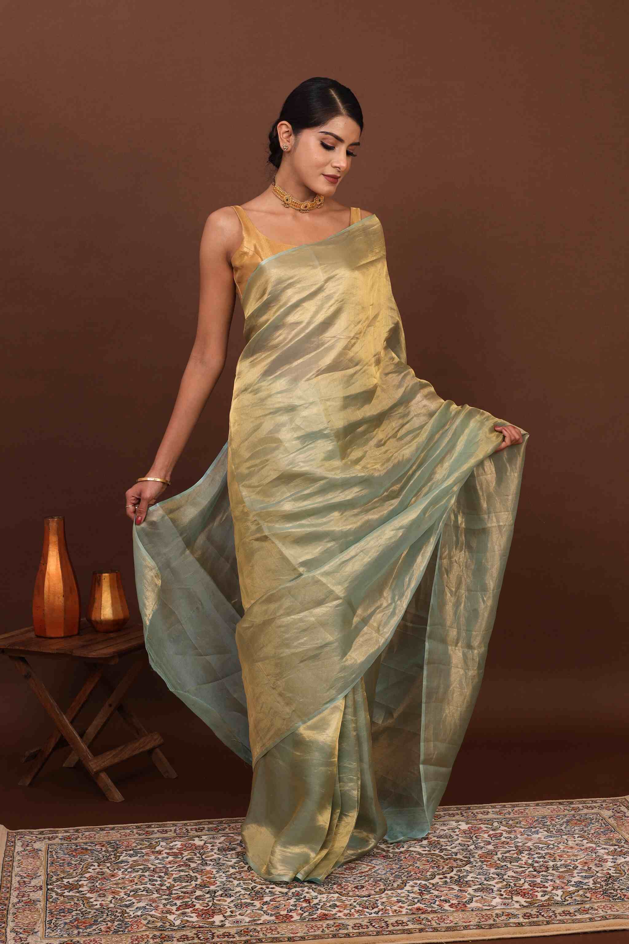 In front View model posing elegantly in green pure tissue silk saree in brown background