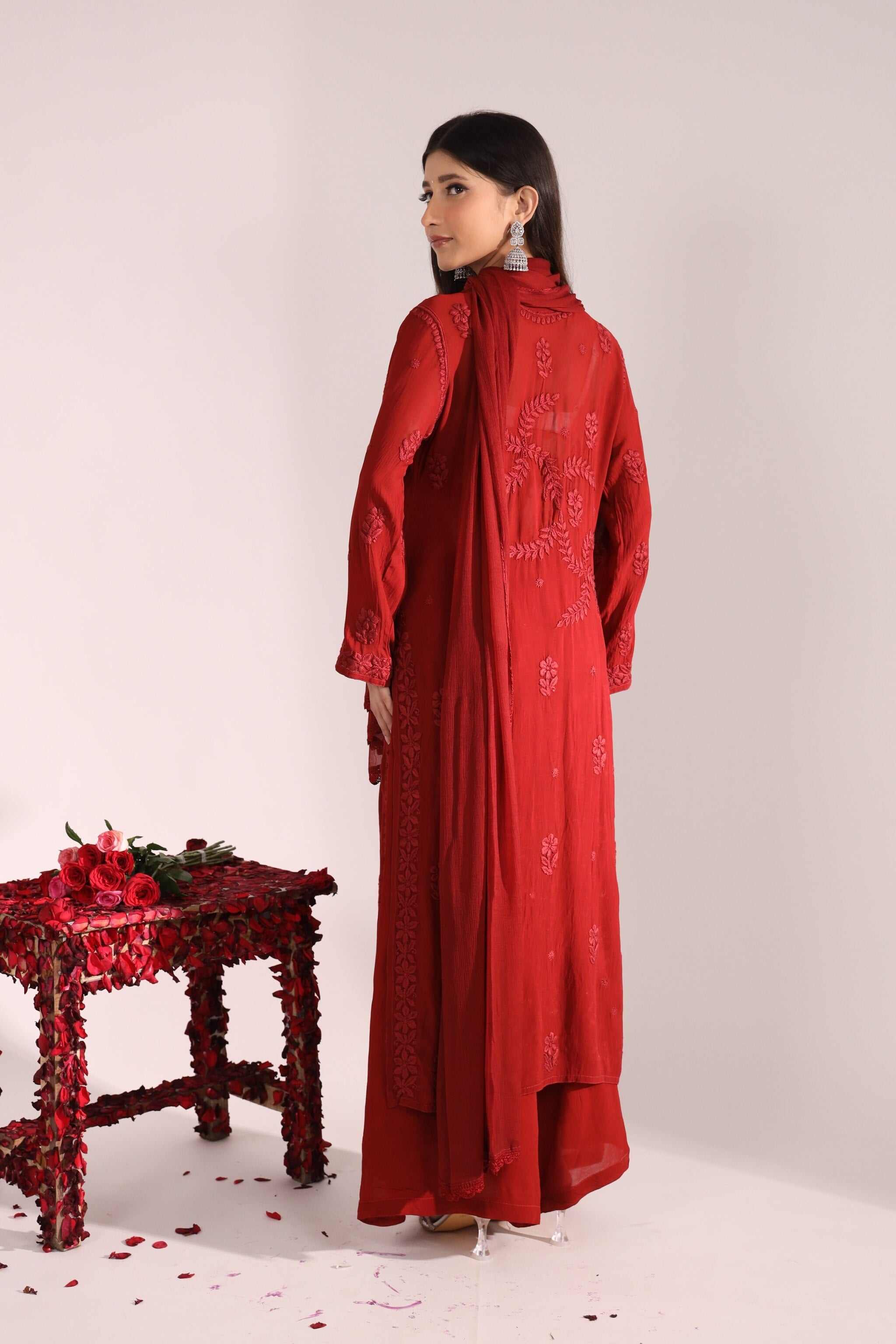 Back view Woman in a red dress standing next to a red table with flowers on a white background