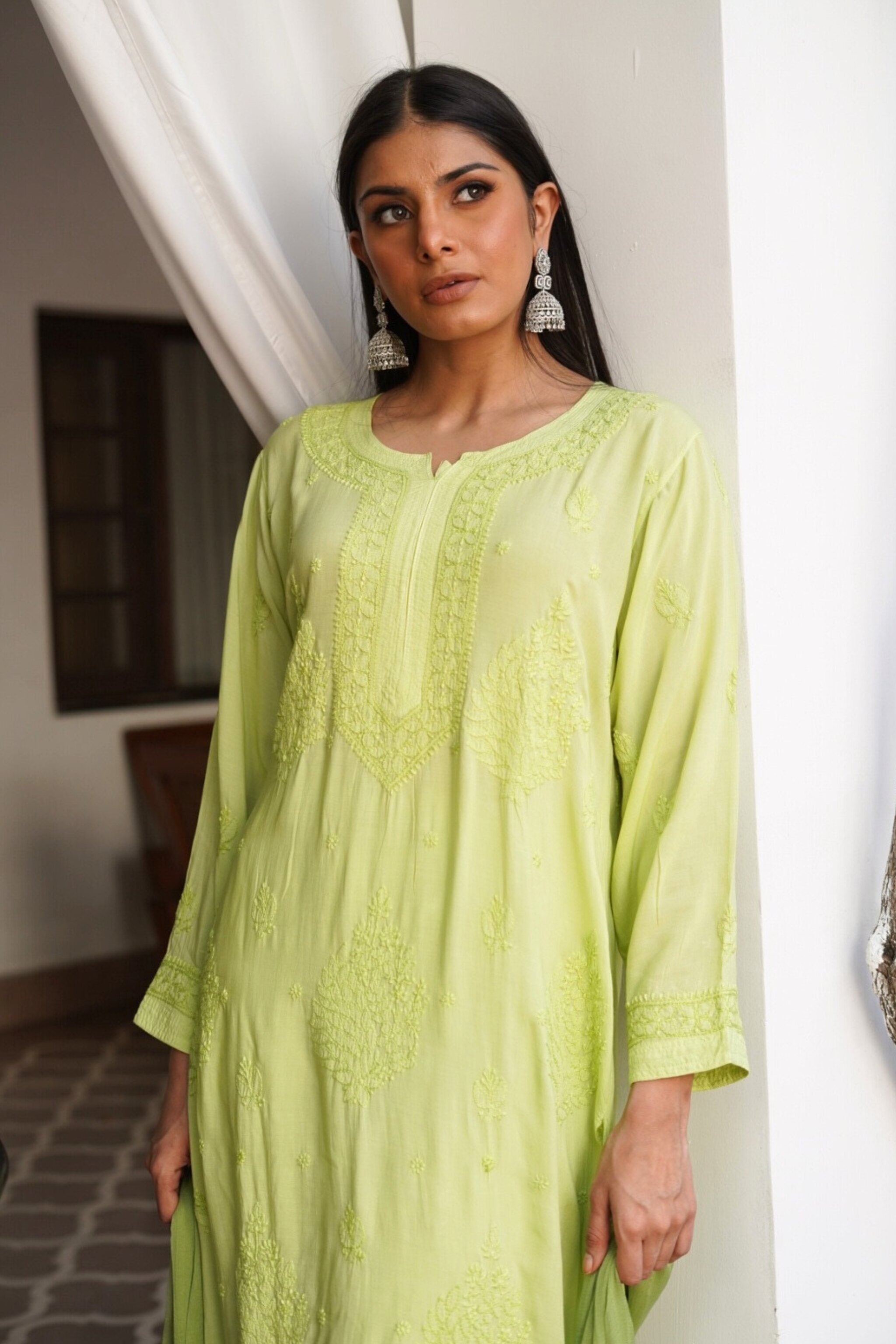 Woman wearing a light green embroidered chikan kurta set indoors.