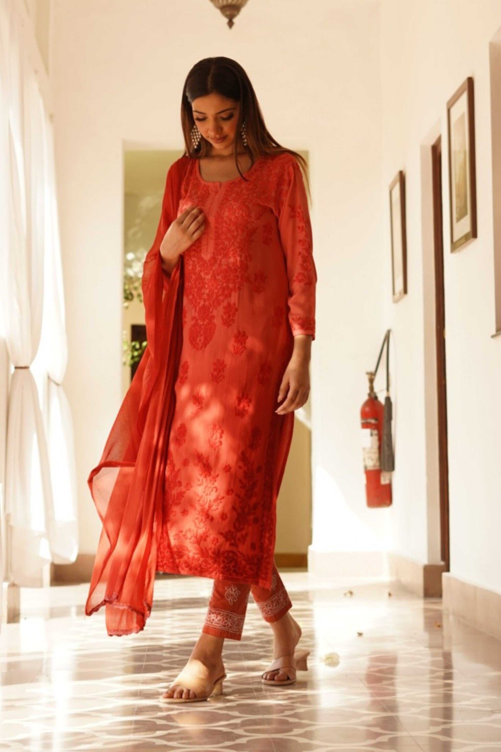 Woman in a red traditional outfit standing in a well-lit room.