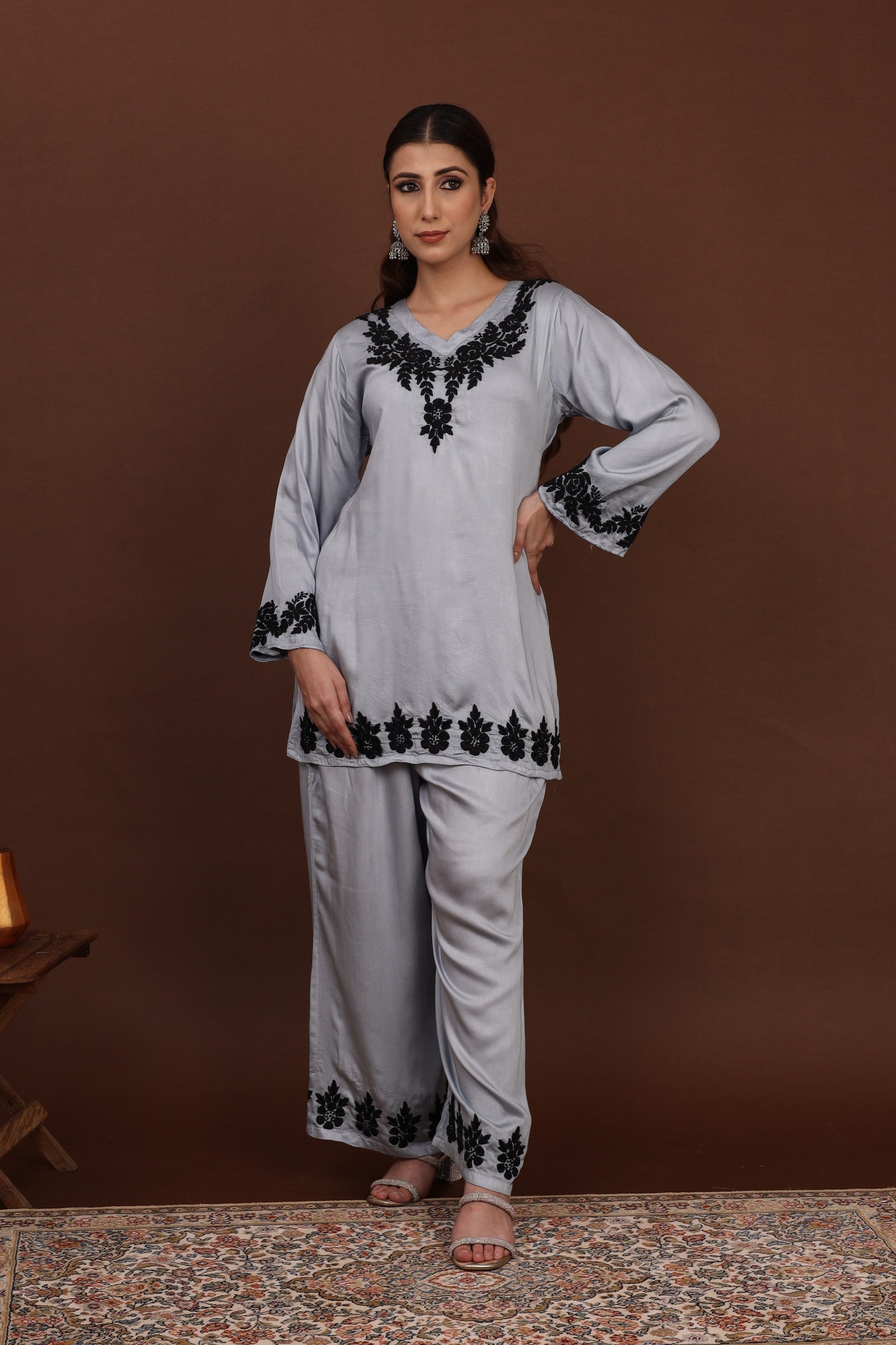 Woman wearing a light gray chikankari co ord set with black embroidery against a brown background