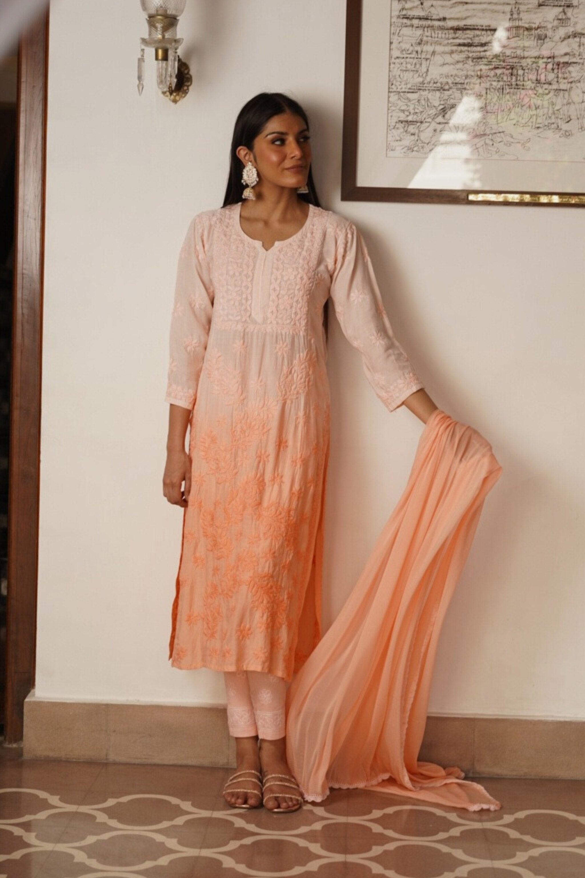 Woman in a peach and pink traditional chikankari kurta set standing indoors.
