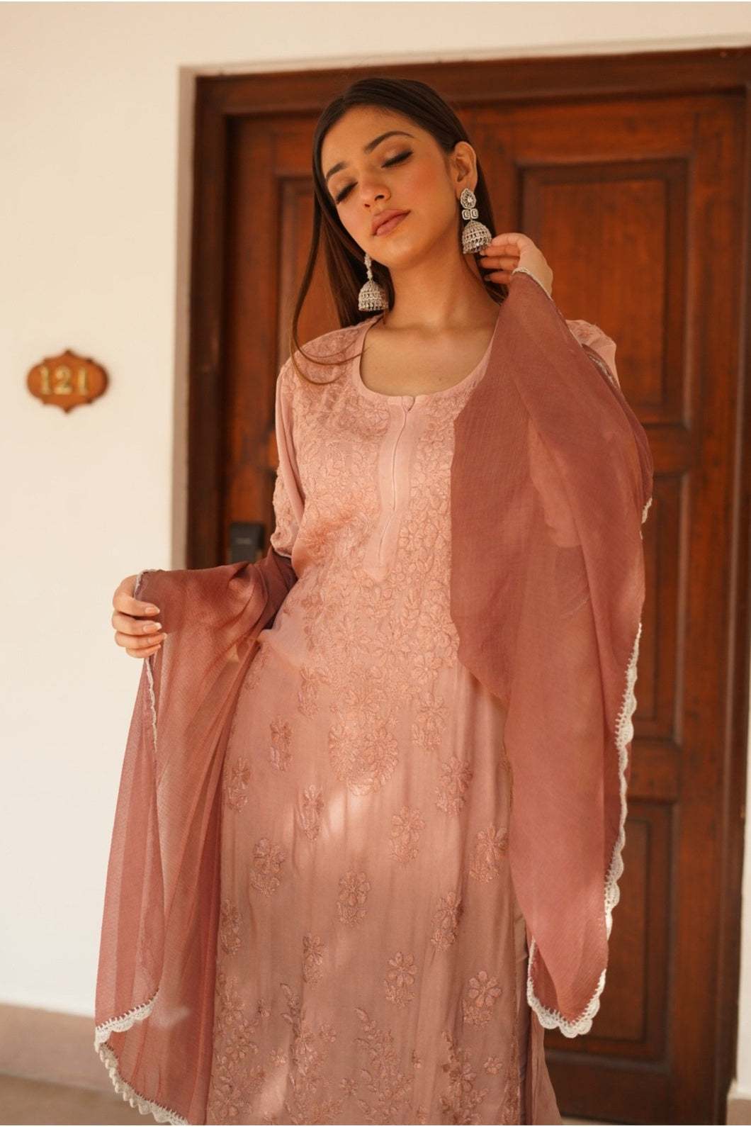 Woman wearing a brown chikakari kurta set with brown dupatta  in front of a wooden door.