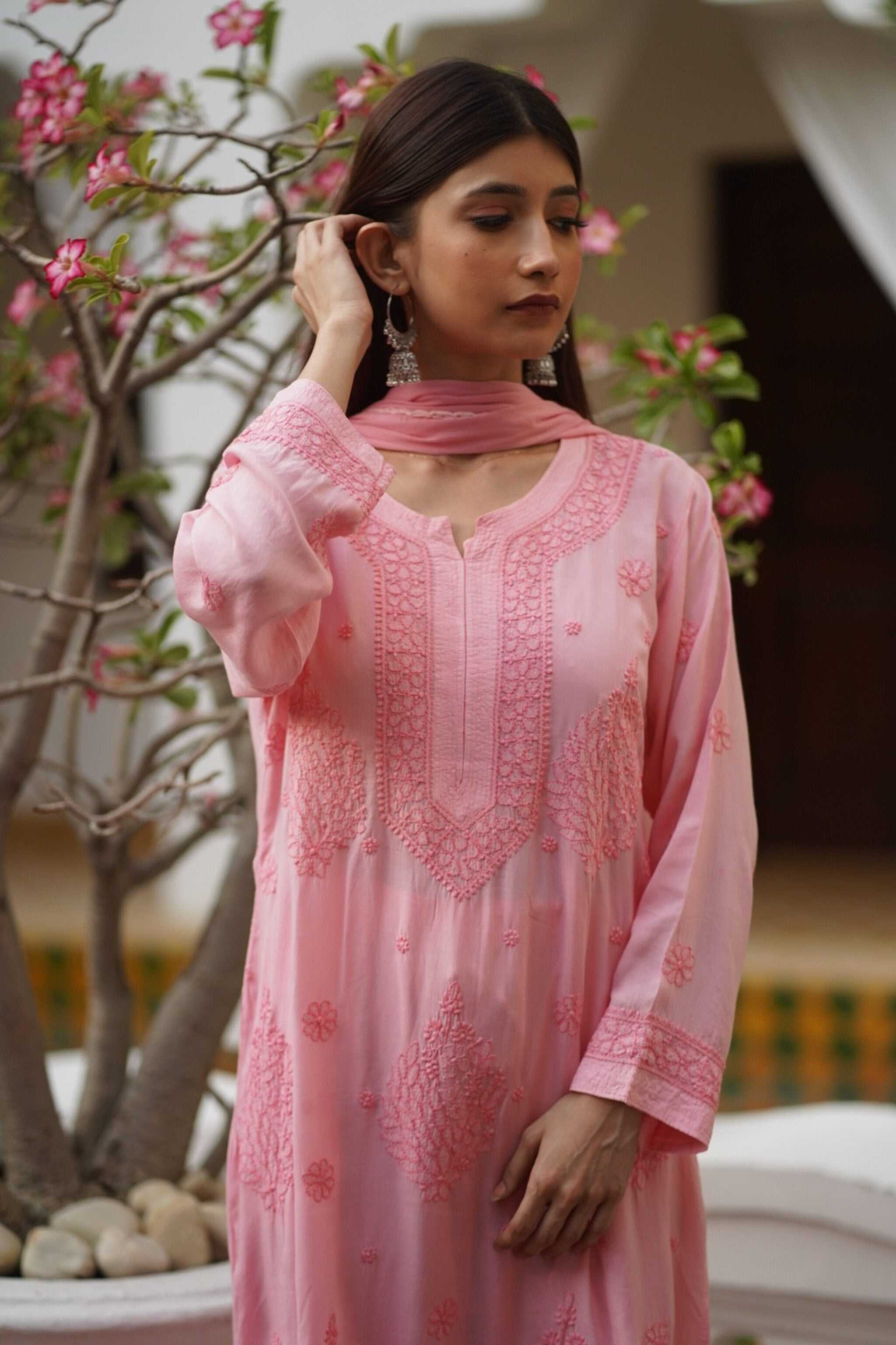 Woman wearing a peach embroidered chikankari kurta set with a blurred floral background