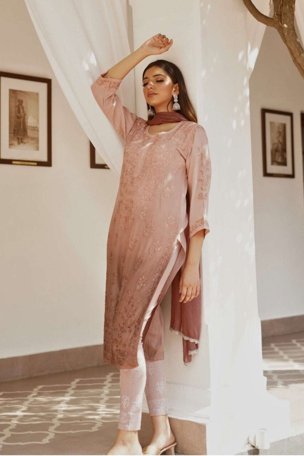 Woman in a pink traditional chikankari kurta set standing indoors with white curtains.