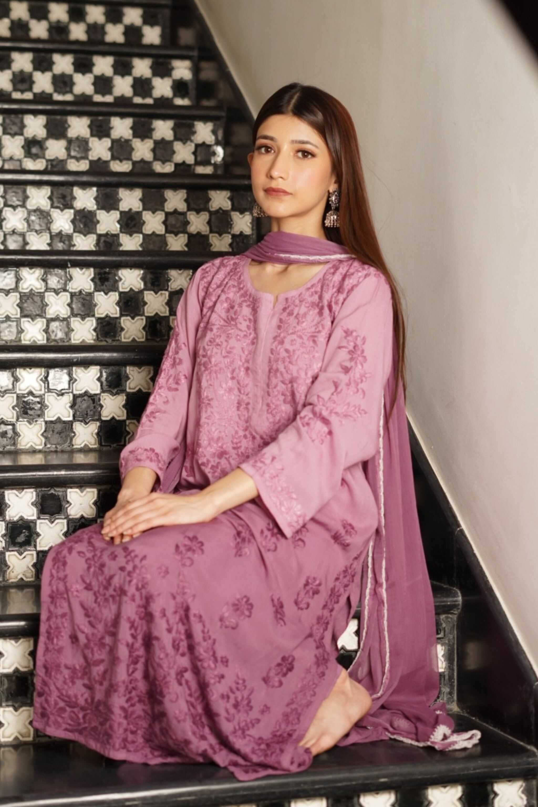 Woman in a pink traditional chikankari suit sitting on a decorative staircase.