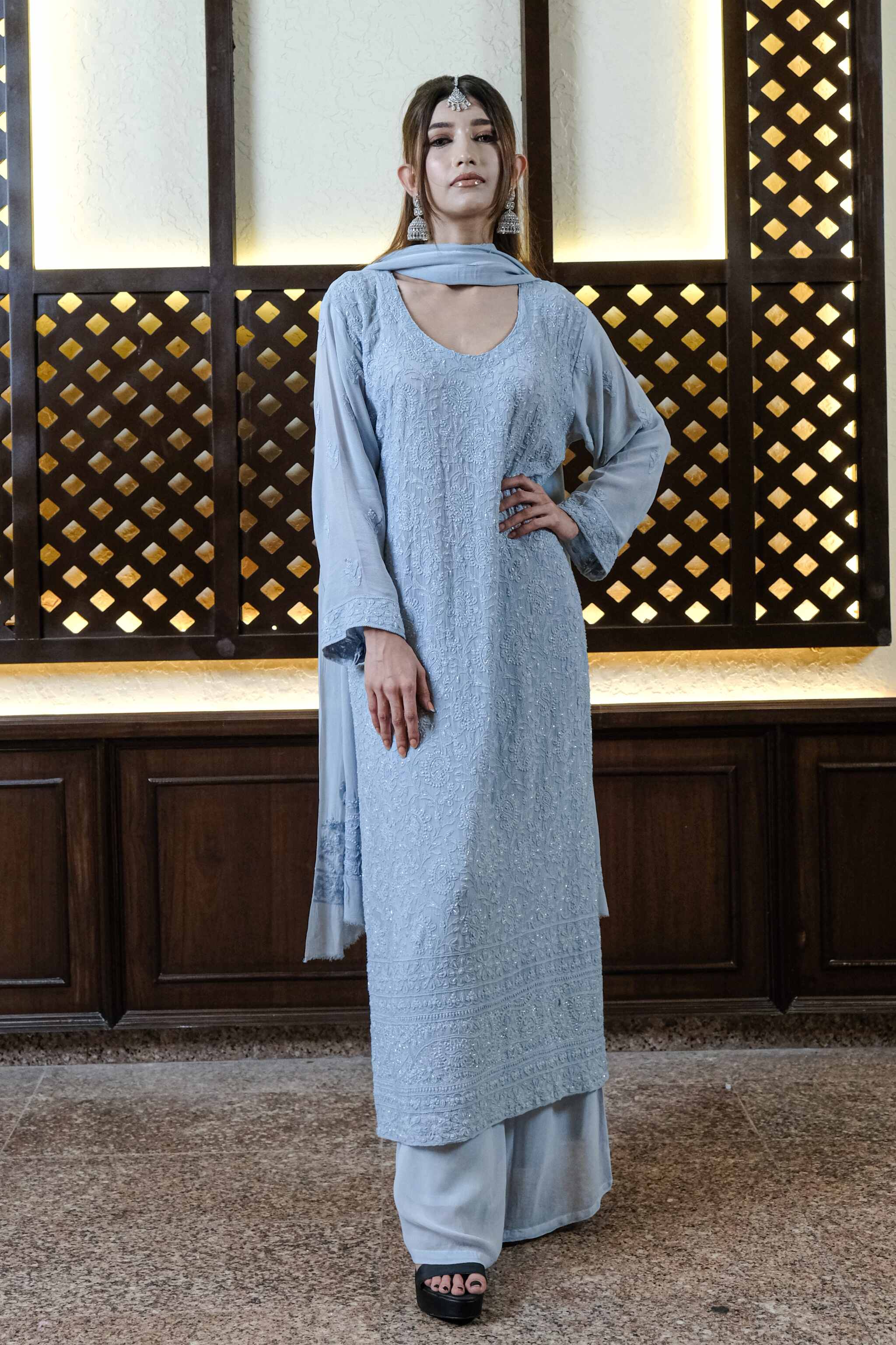 Woman wearing a light blue traditional Chikankari Wedding Suit for Women in an indoor setting with decorative wall.