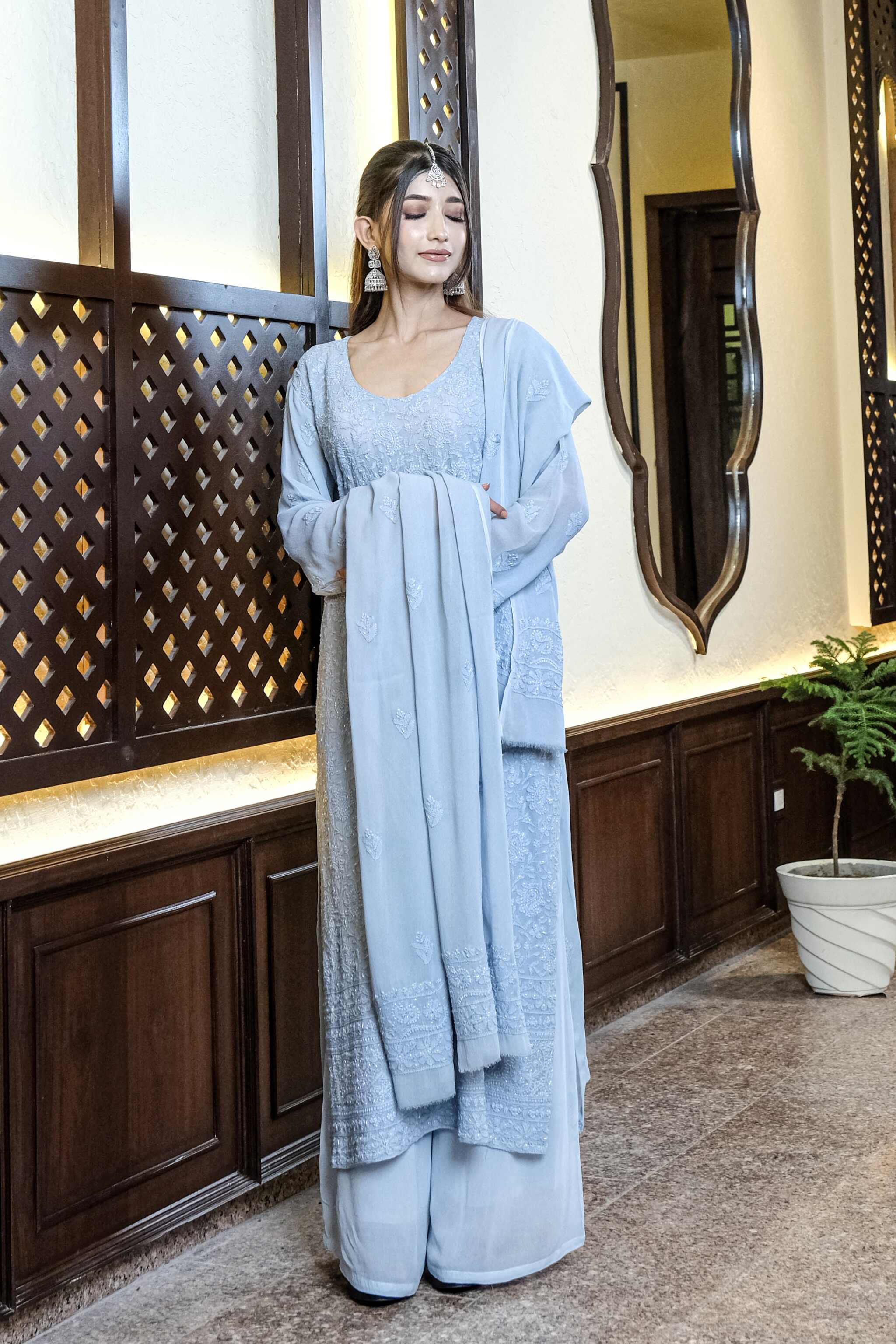 Woman in a light blue traditional chikankari wedding suit standing in a decorative interior setting.