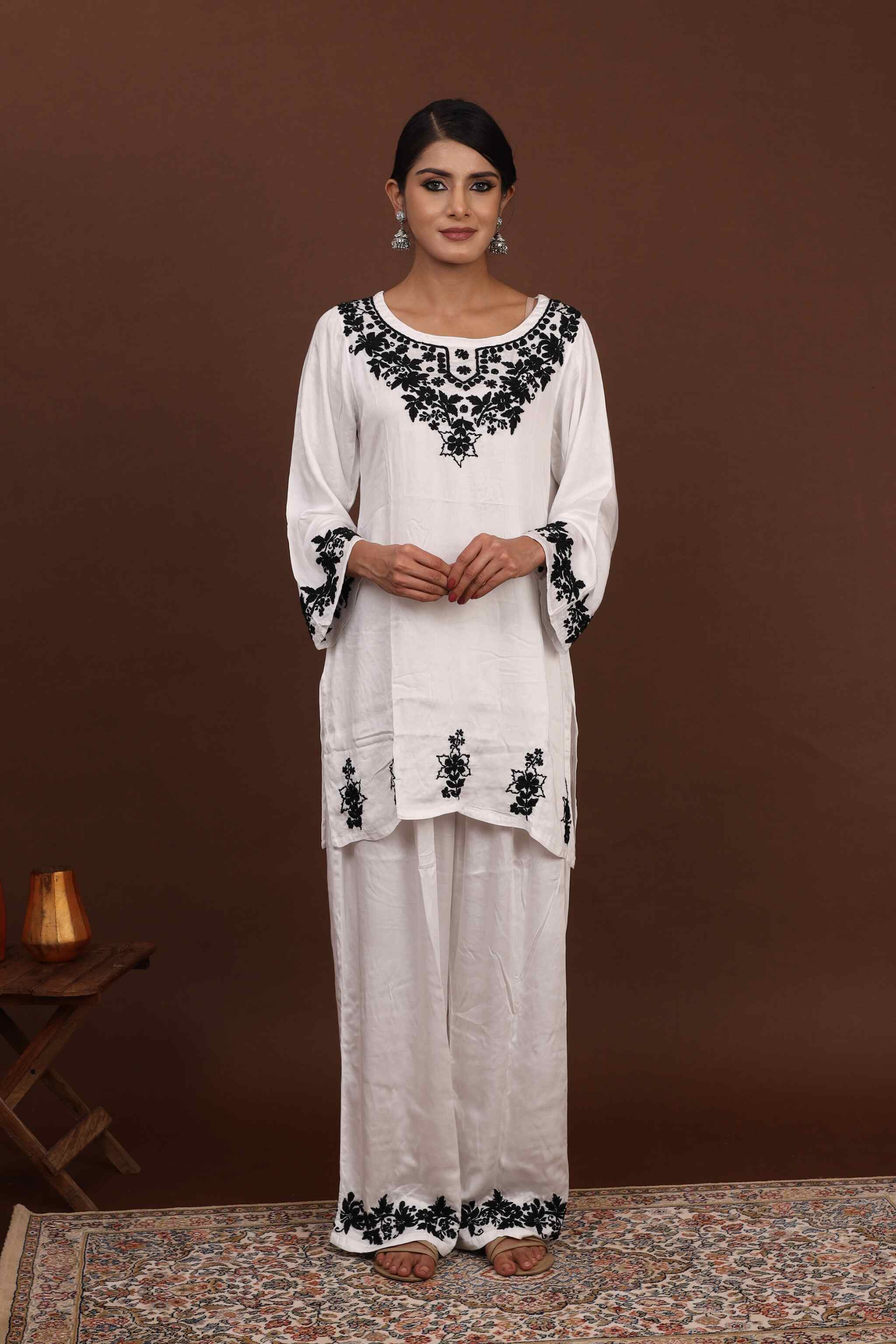 Woman wearing a white co ord set with black embroidery against a brown background