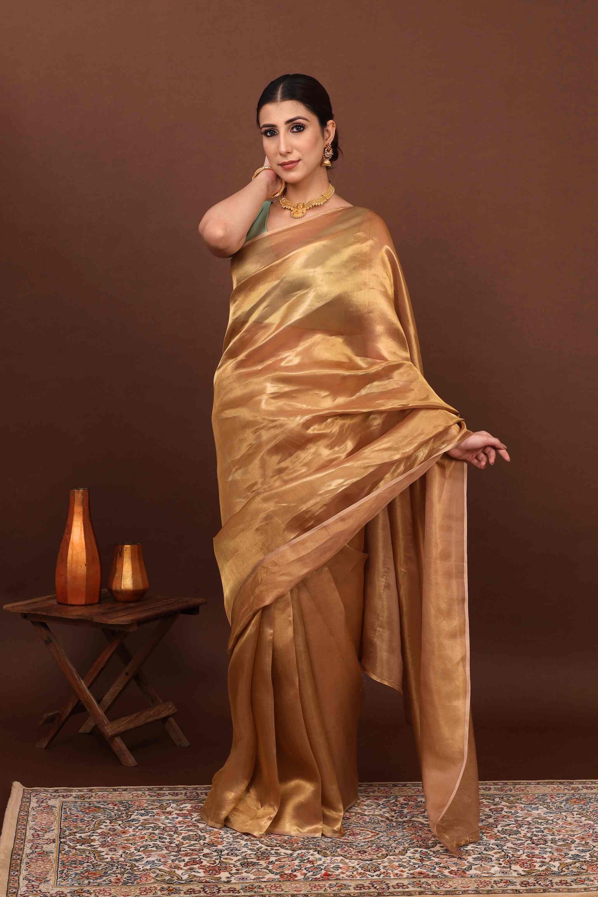 In fron view model posing elegantly in golden tissue saree in brown background