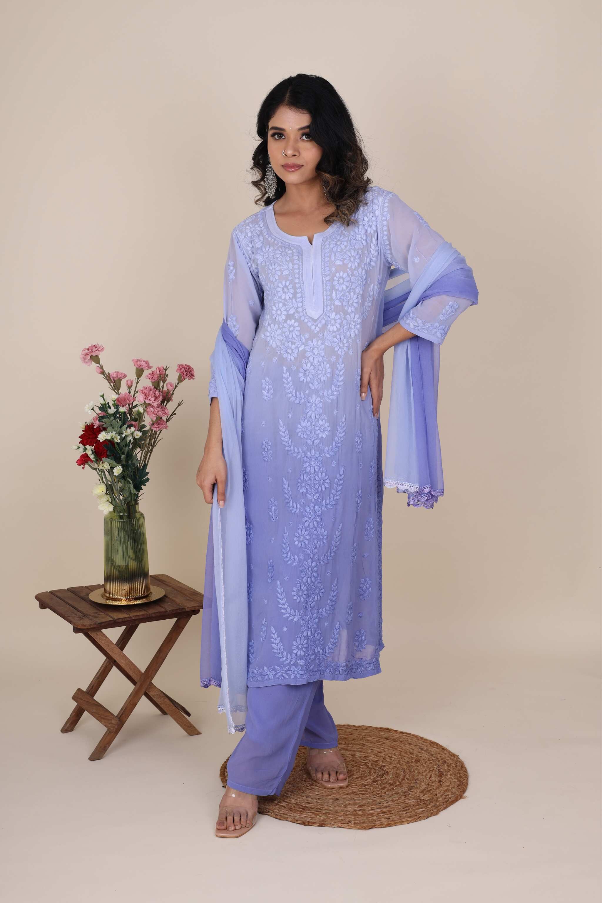Woman wearing a light blue embroidered chikankari Heer topaz set with a floral arrangement on a beige background
