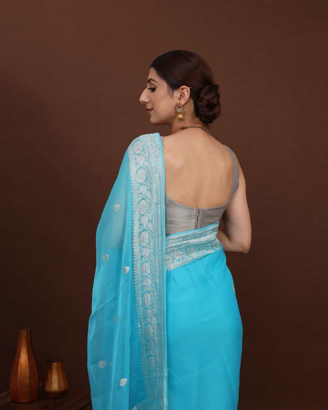 Woman wearing a light blue khaddi georgette banarasi
saree with a brown background  