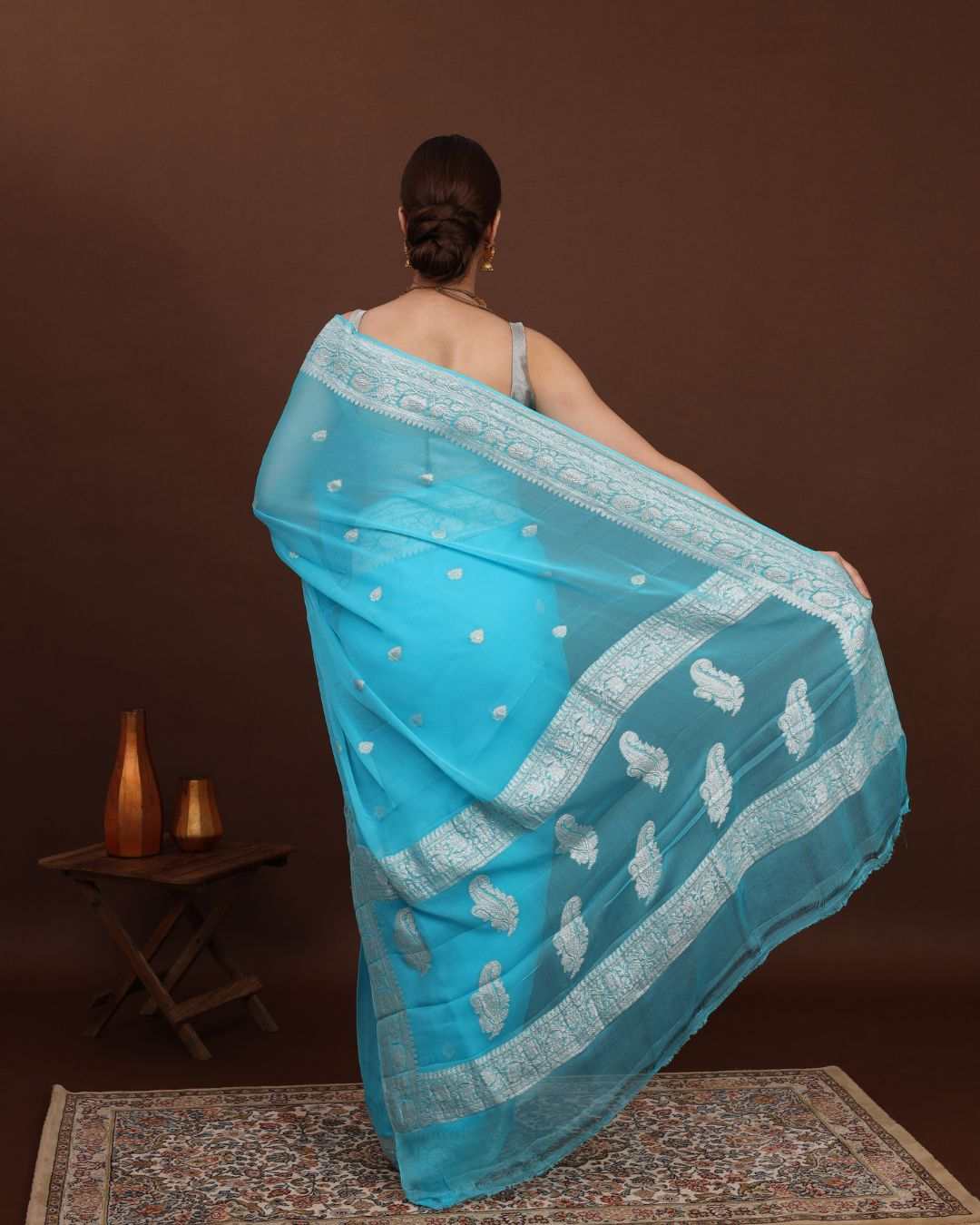 women wearing a khaddi georgette banarasi saree showing a back pallu which is weaved with silver zari in a dark background