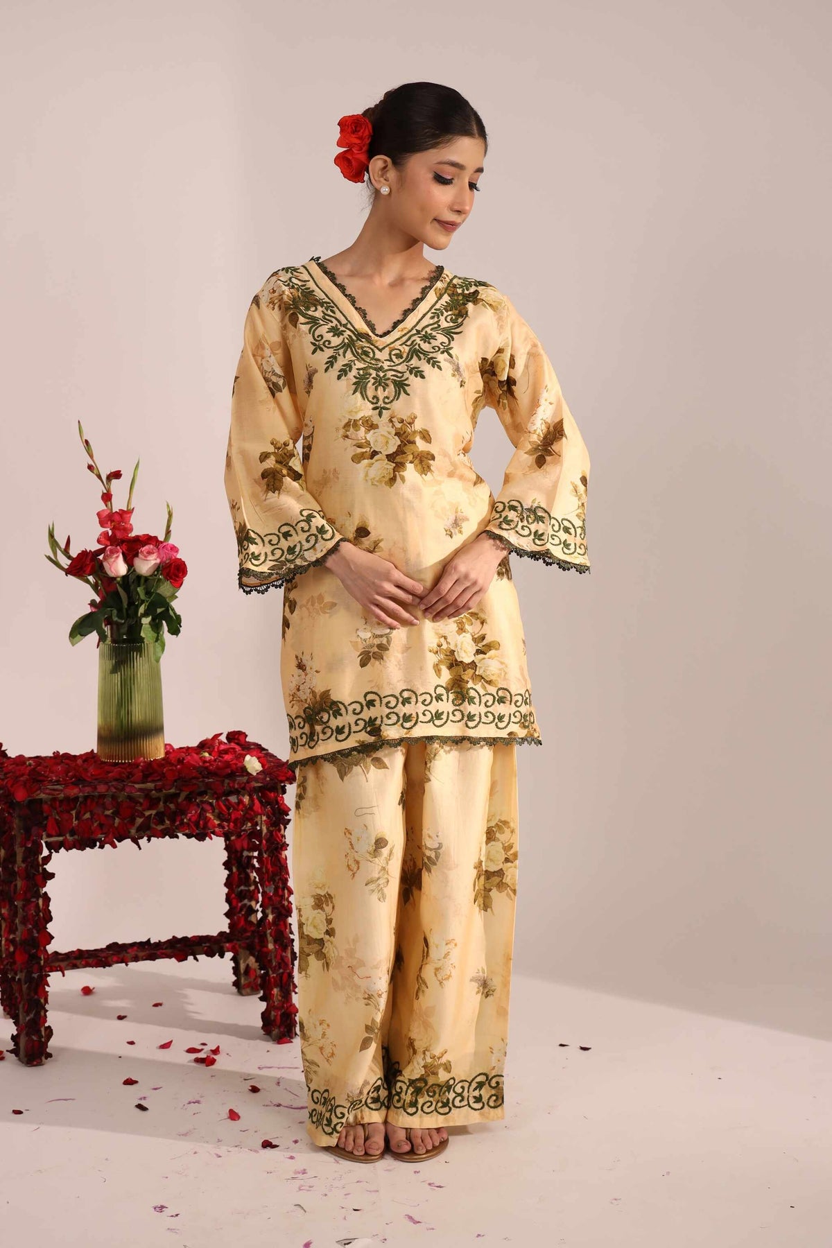 Woman in a Senorita beige floral chikankar chanderi co ord set with floral decorations, standing next to a small table with flowers.