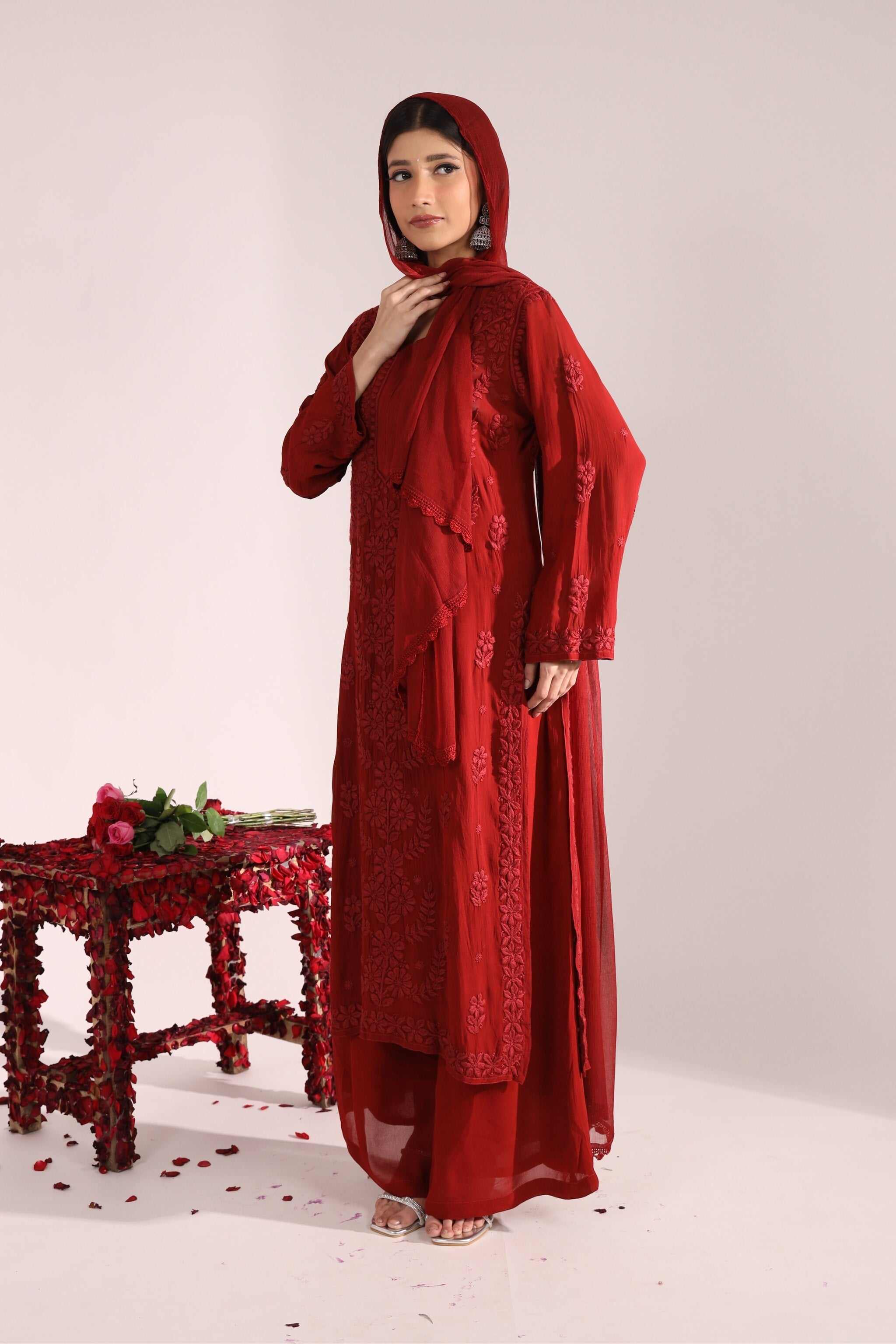 Woman wearing a red embroidered chikankari set with a matching dupatta on a white background