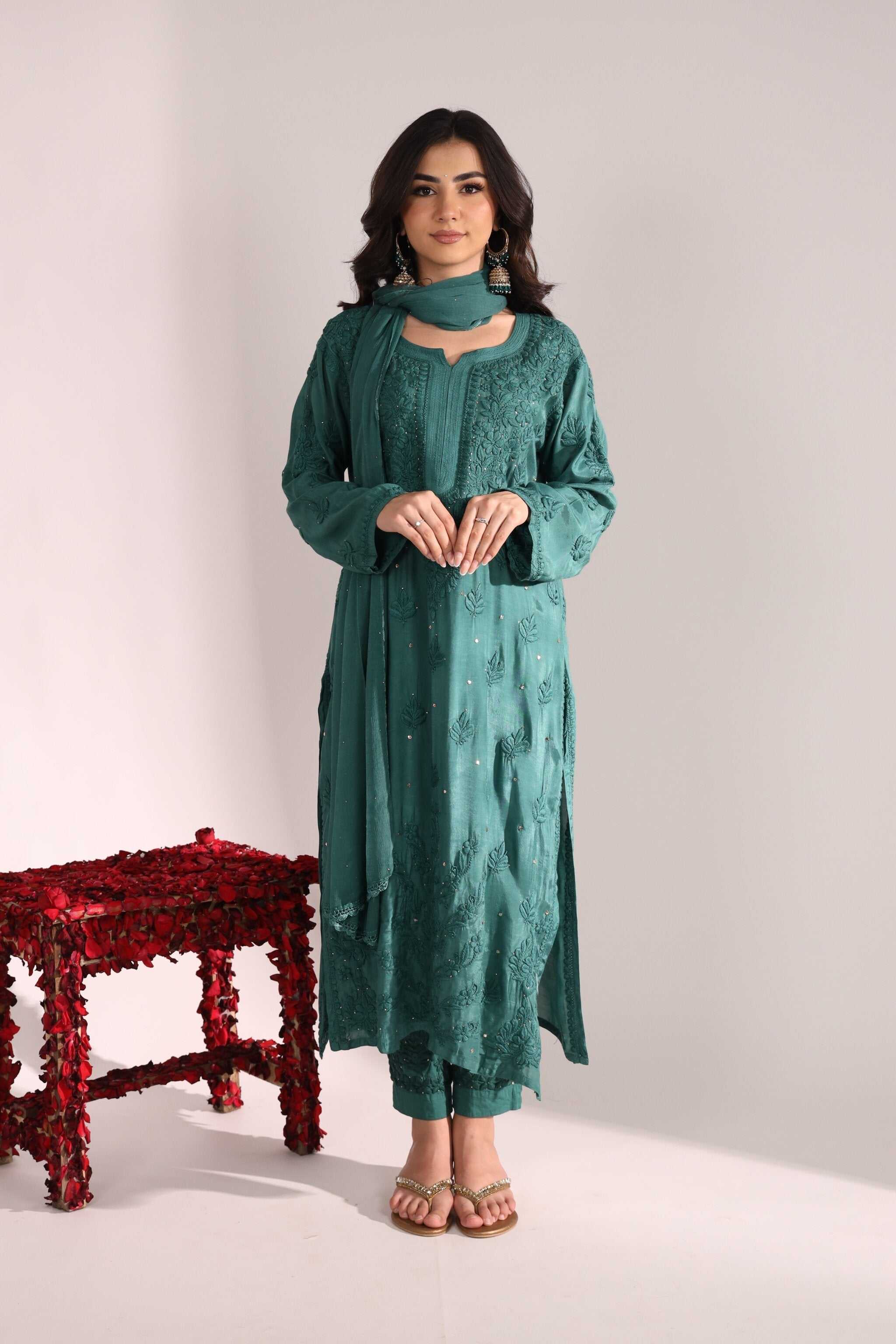 Woman wearing a teal Sitara Sanchi Chikan Kurta Set standing next to a red stool on a white background