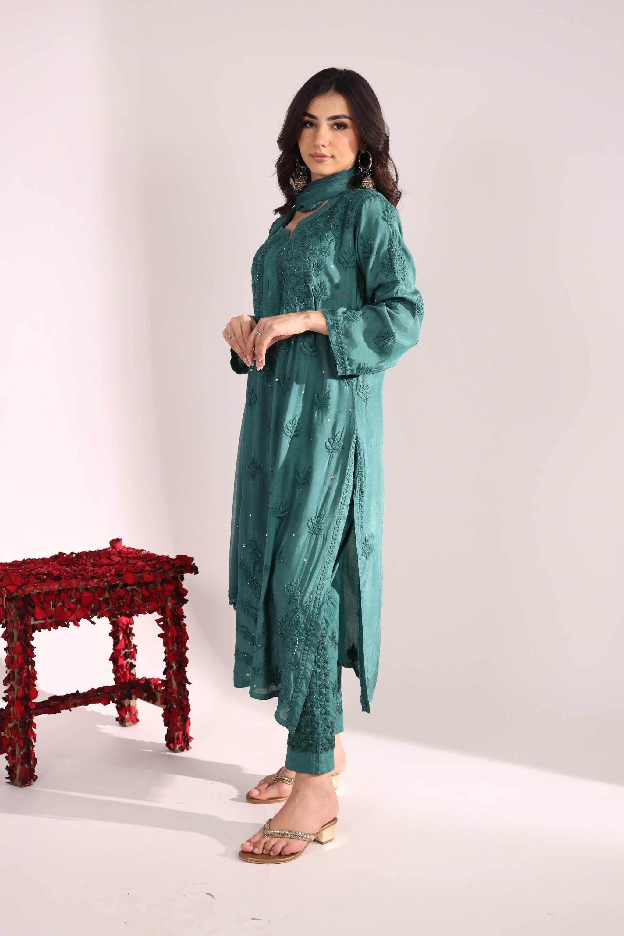 Woman wearing a teal Sitara Sanchi Chikan Kurta Set standing next to a red stool on a white background