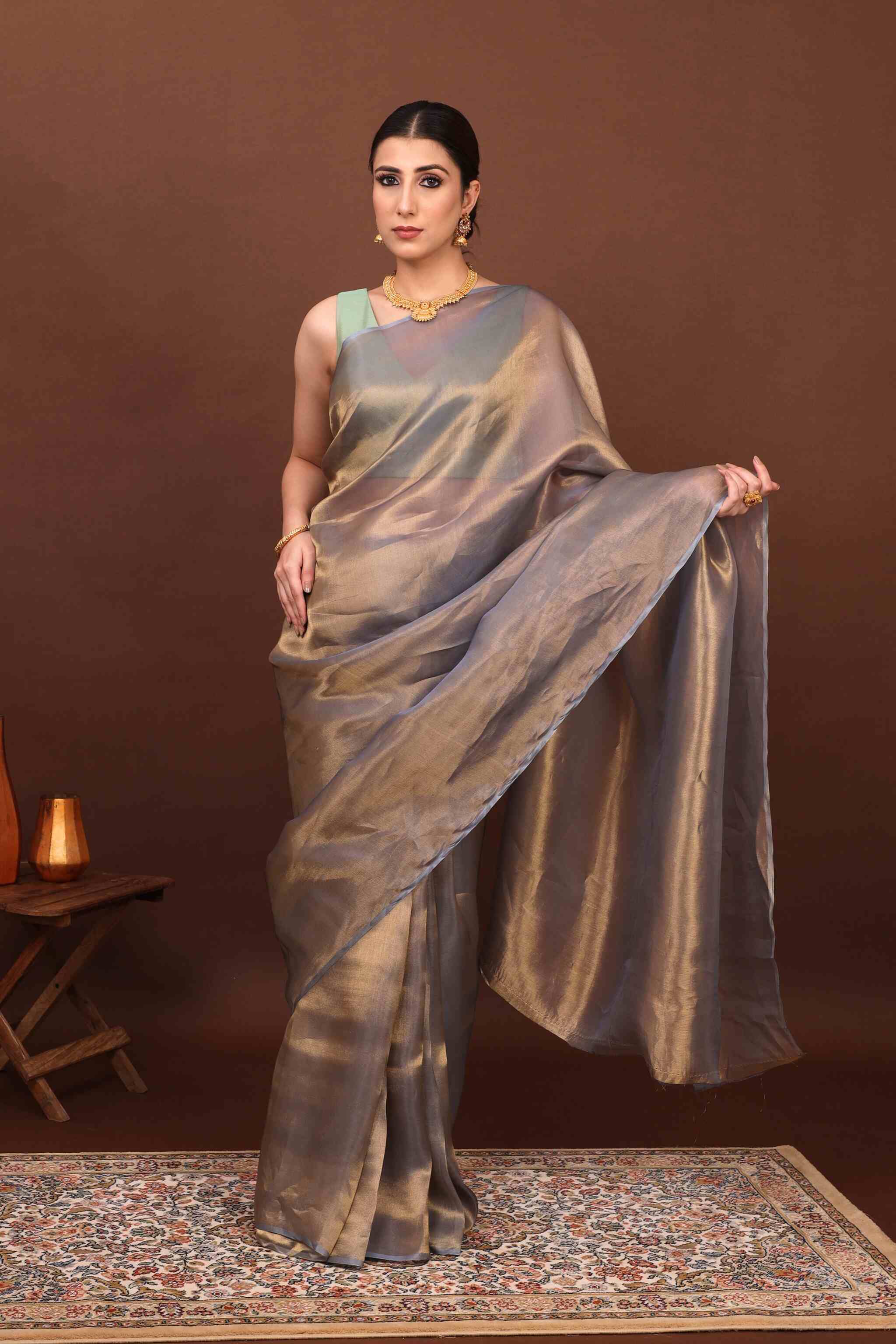 In Front view model elegantly posing in teal grey tissue saree in brown background