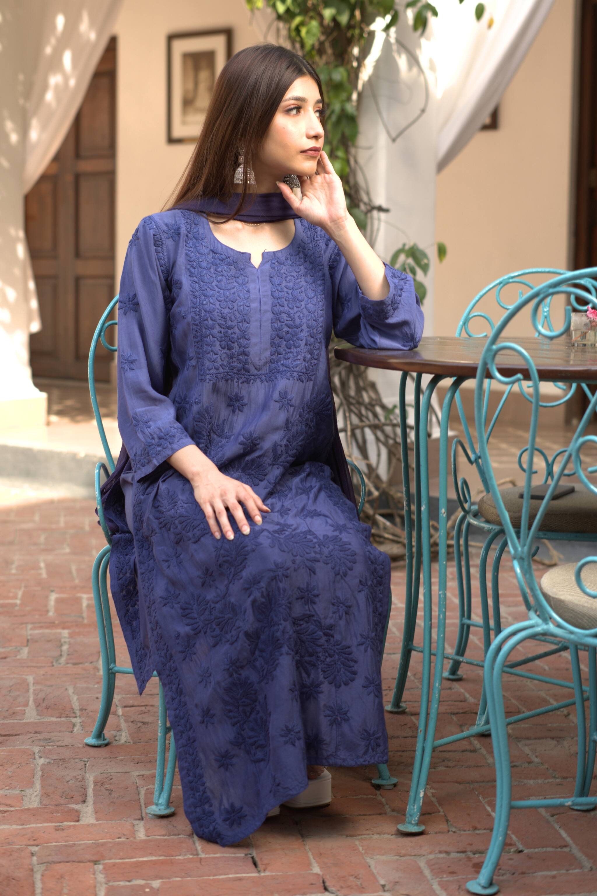 Woman in a blue chikankari kurta set sitting at an outdoor cafe table.
