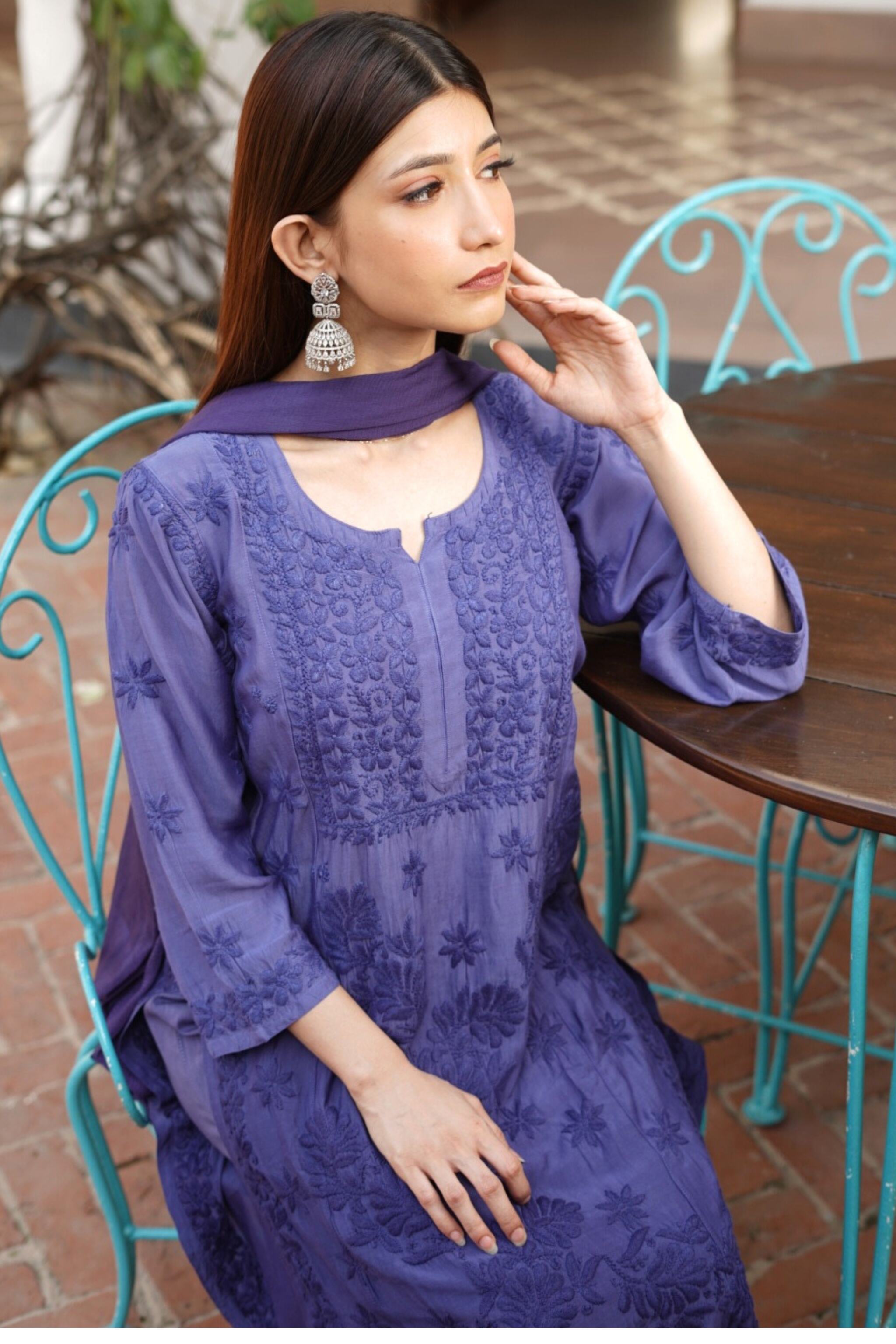 Woman in a purple embroidered chikankari kurta set sitting outdoors at a table.