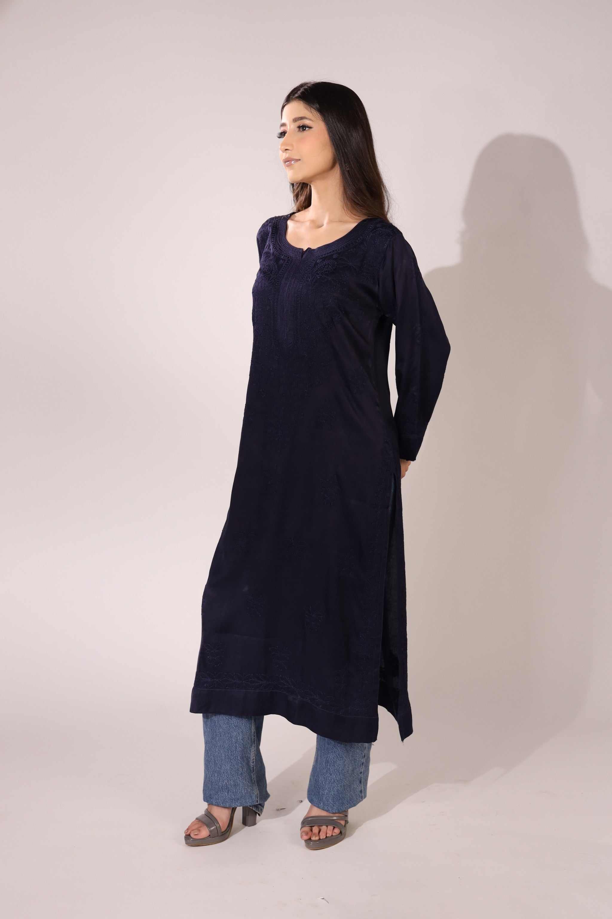 Woman wearing a long navy blue lucknowi kurti with blue jeans against a white background