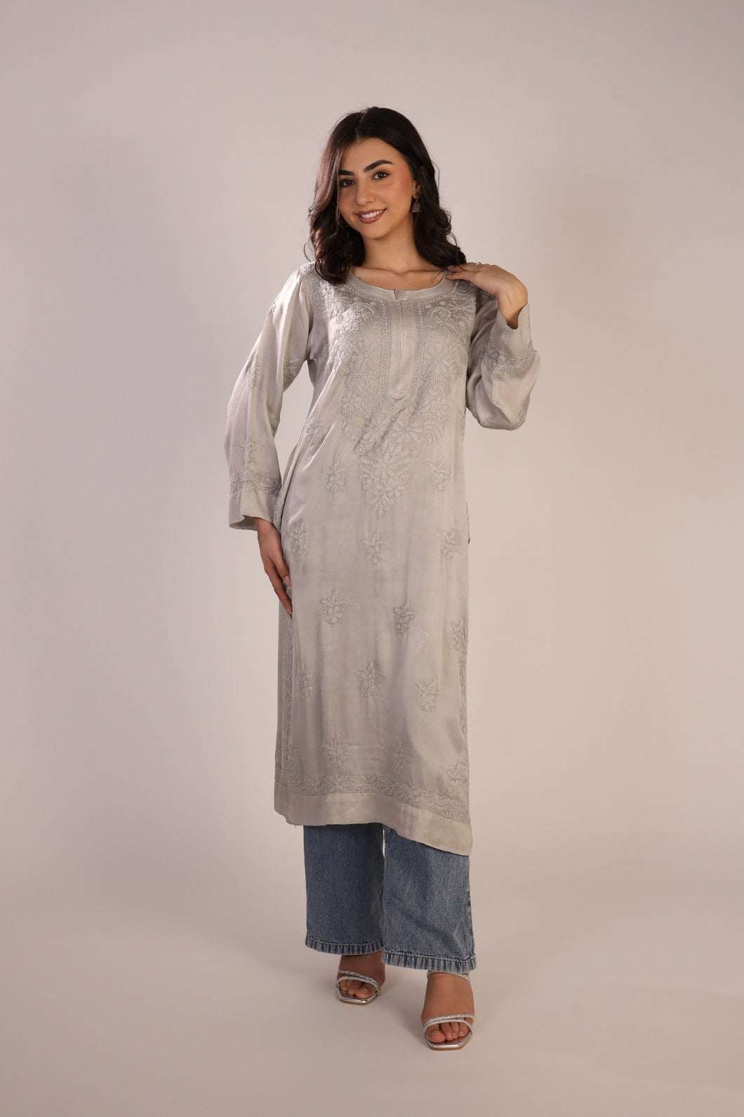 Woman wearing a long light-colored chikankari kurta with denim pants on a plain background