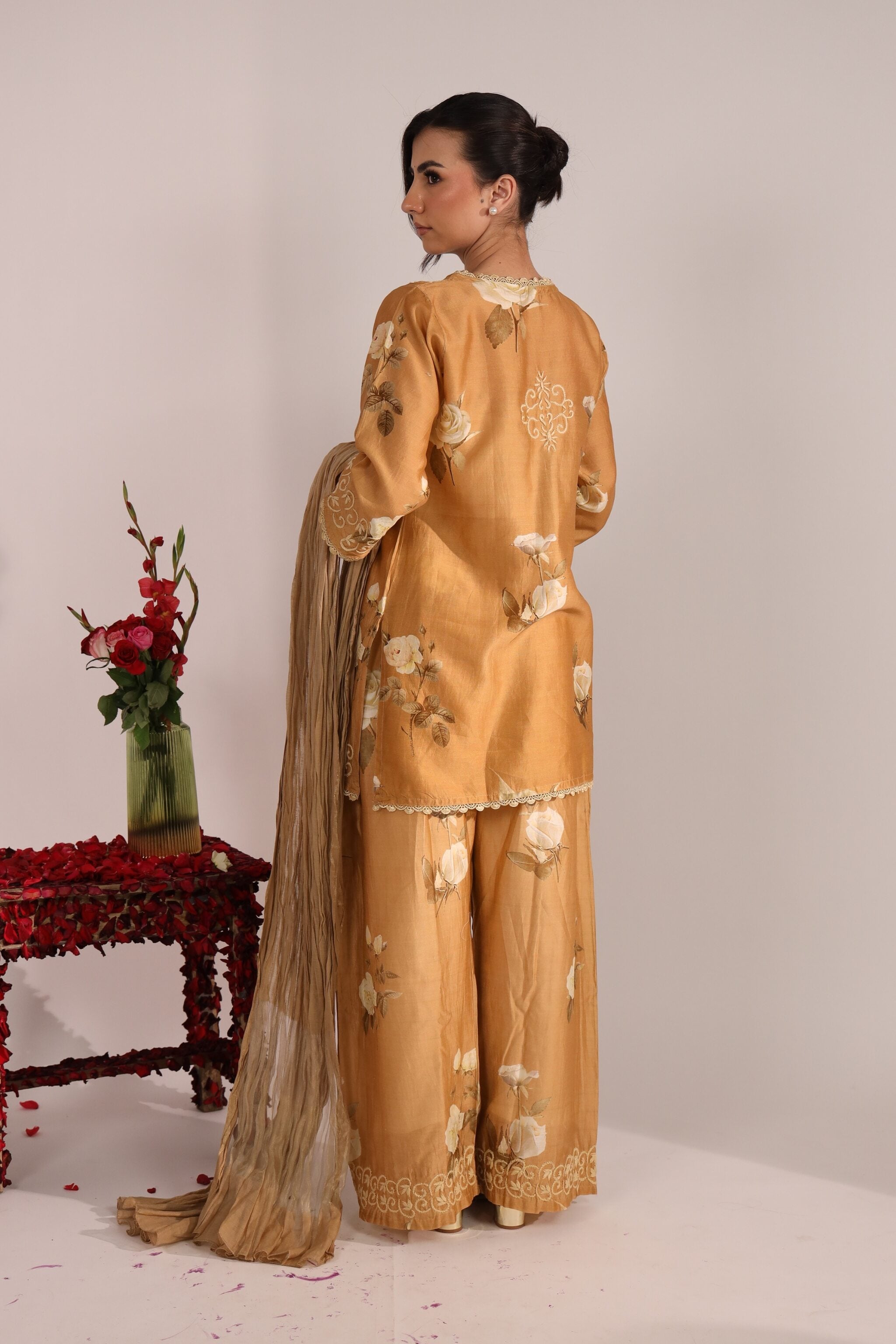 Woman in a mustard yellow traditional co ord with floral patterns, standing against a plain background.