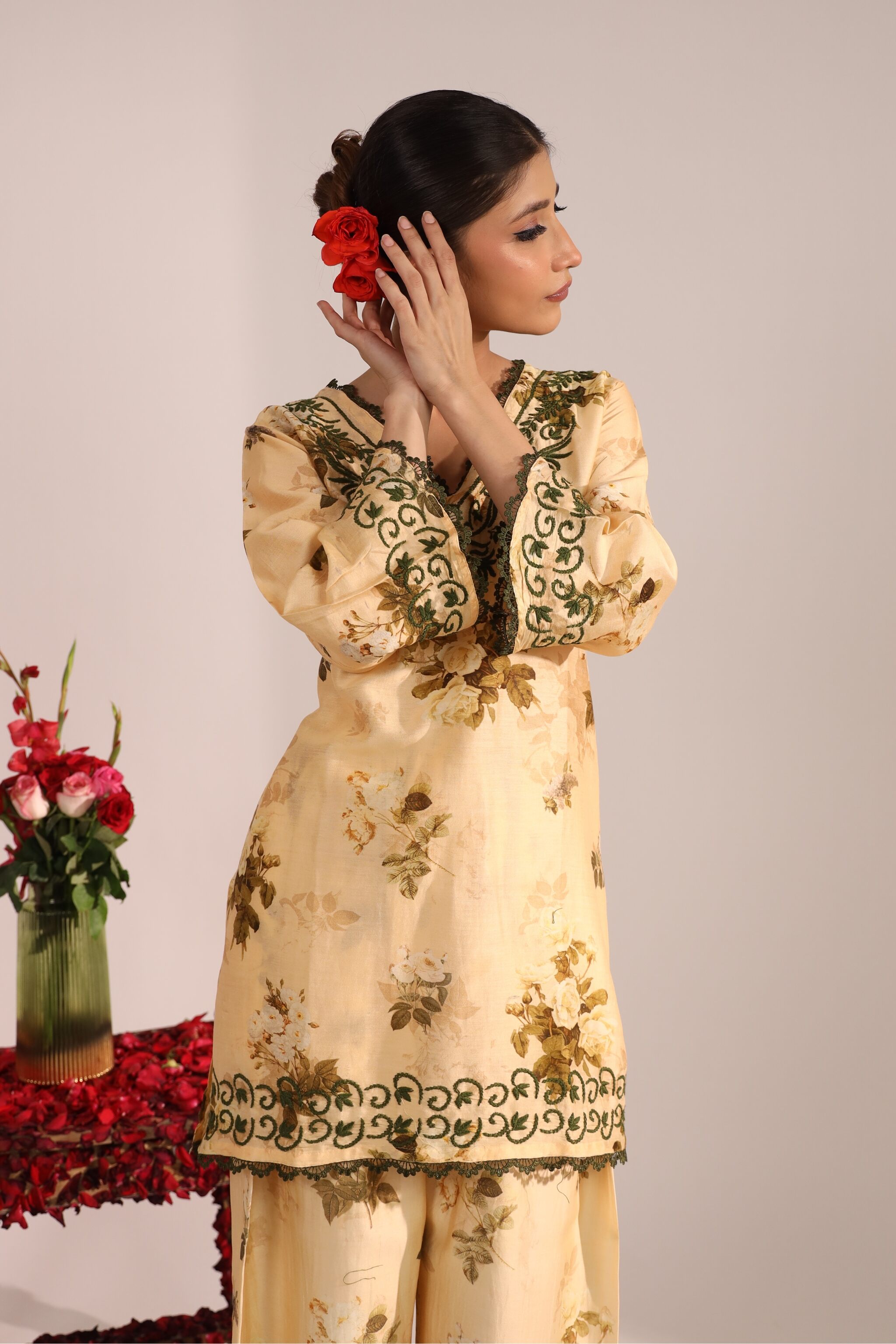 Woman wearing a printed yellow co ord Sanorita chikankari embroidered set with a vase of flowers in the background
