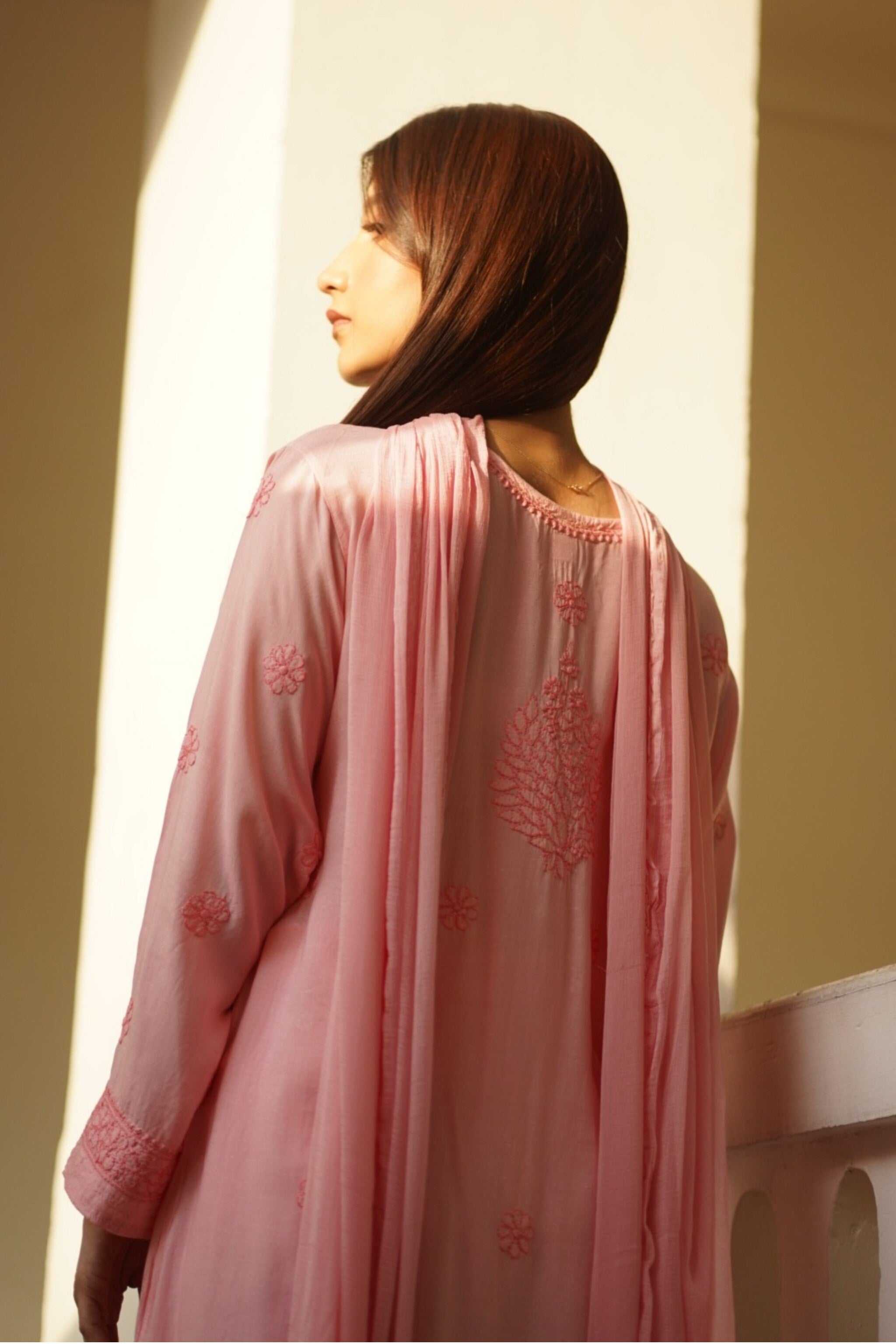 Woman wearing a peach embroidered chikankari kurta set against a neutral background