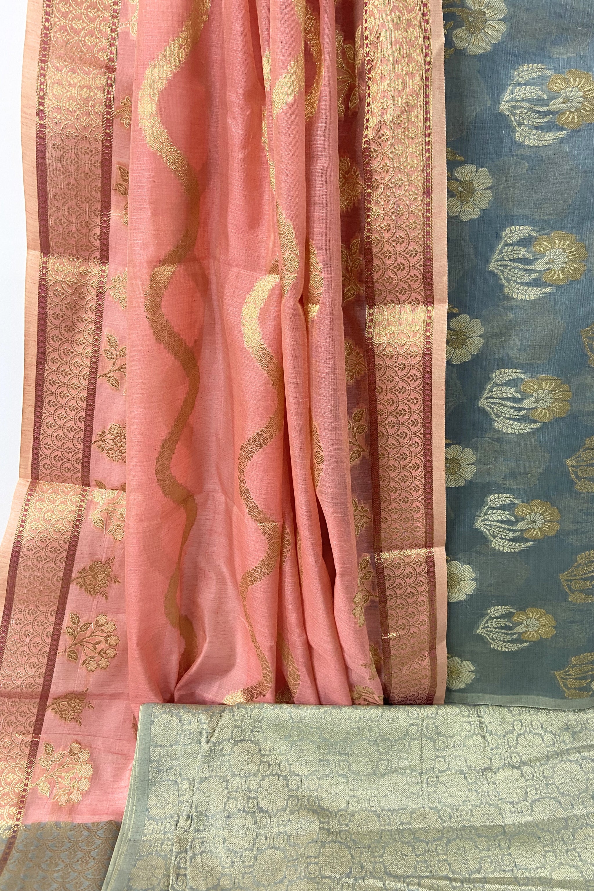 A close-up of a traditional Indian silk suit  fabric set featuring a gazari pink dupatta with gold zari motifs, a blue-gray floral patterned kurta fabric, and a light sage green brocade salwar fabric  with gold zari work.